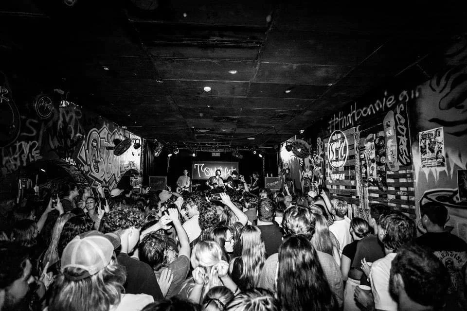 Crowd of people at an indie live gig at Tomcat- a live music grunge bar with graffiti-covered walls and red neon lights.