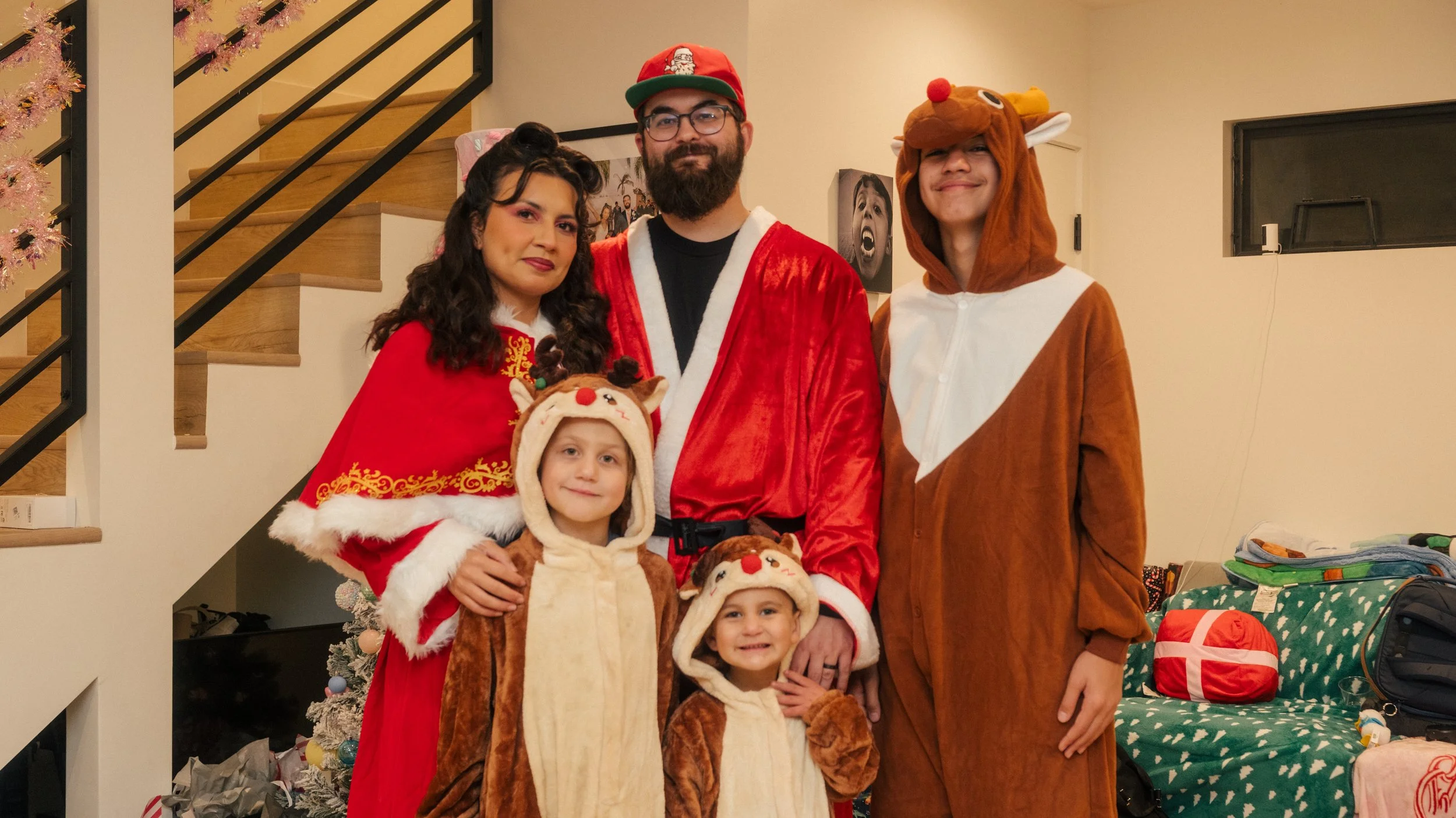 Family dressed in Christmas costumes posing indoors, with children in reindeer and Christmas-themed outfits, and adults in Santa Claus and reindeer costumes.