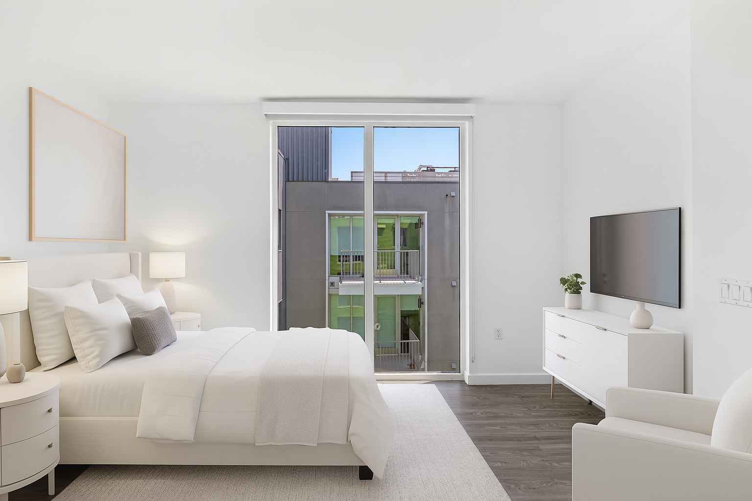 Modern, minimalistic bedroom with white furniture, large bed, and a balcony view, decorated with a potted plant and a flat-screen TV.