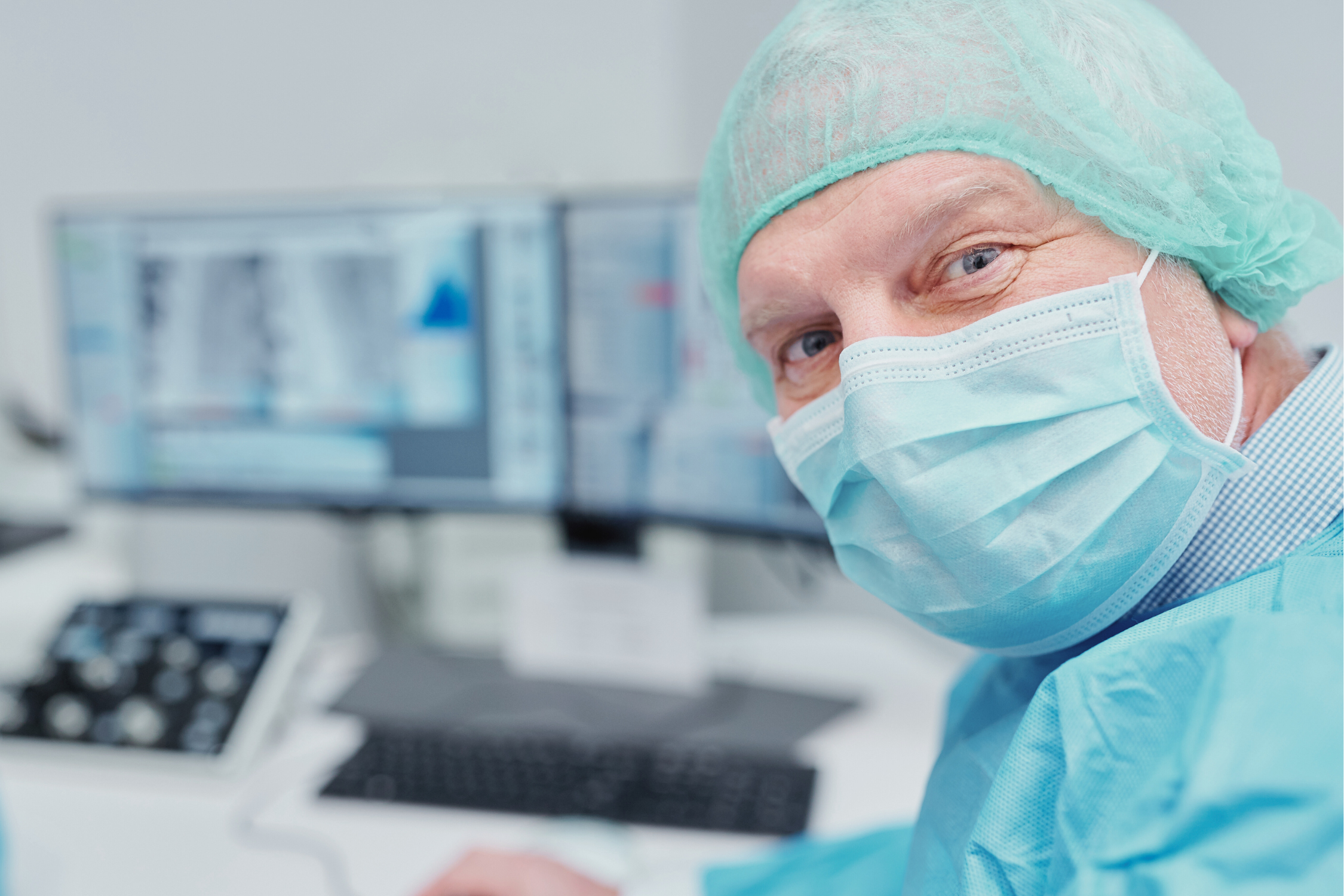 Researcher in surgical attire working with data on multiple screens, representing human researchers conducting trials and gathering comprehensive data for research interventions.