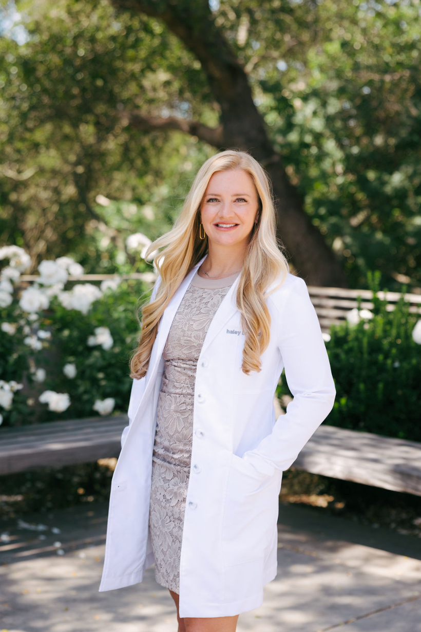 Dr Haley Bray, facial plastic surgeon and medical Director of Graceful Medical Aesthetics in Roseville, California, smiling outdoors in a white medical coat.