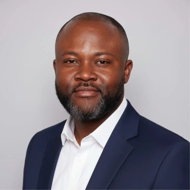 Headshot of a man with a beard, wearing a navy suit and white shirt against a plain light background.