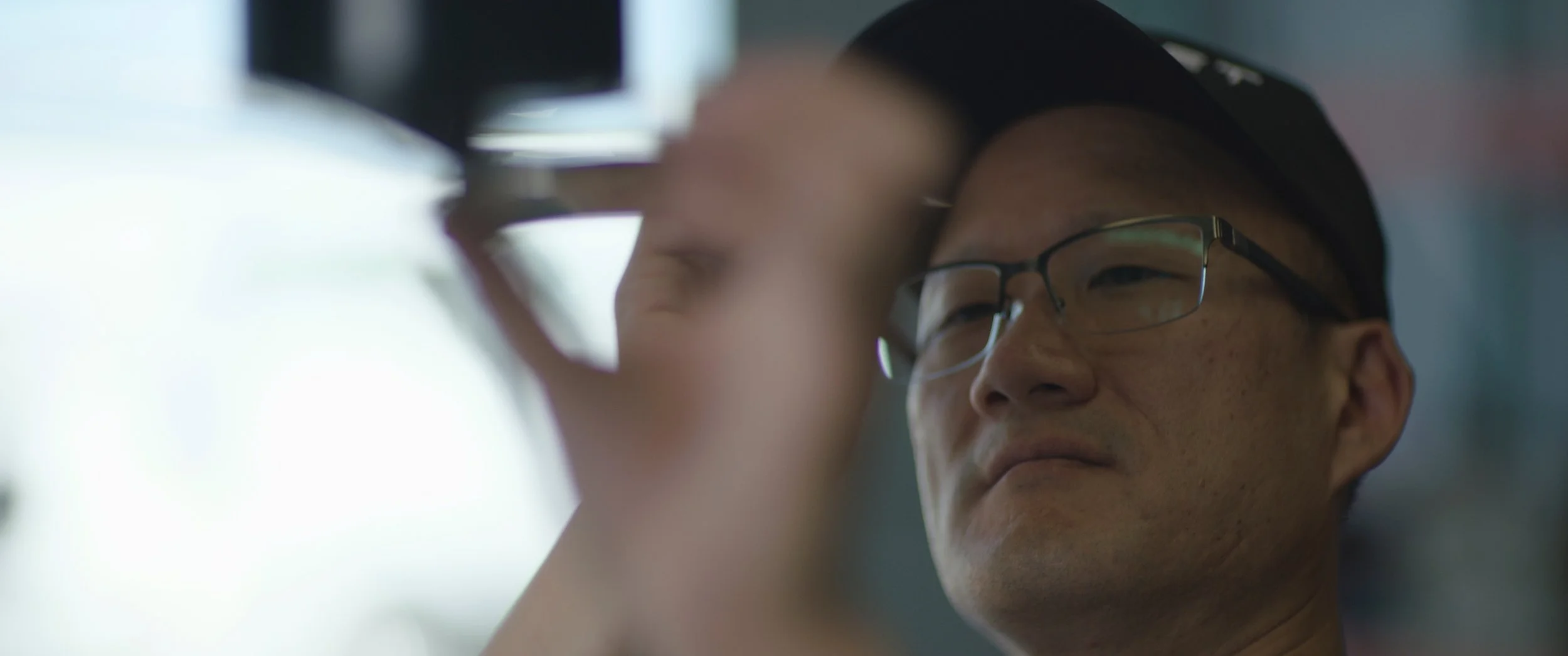 A person adjusting a camera, wearing glasses and a black cap, with a focused expression.