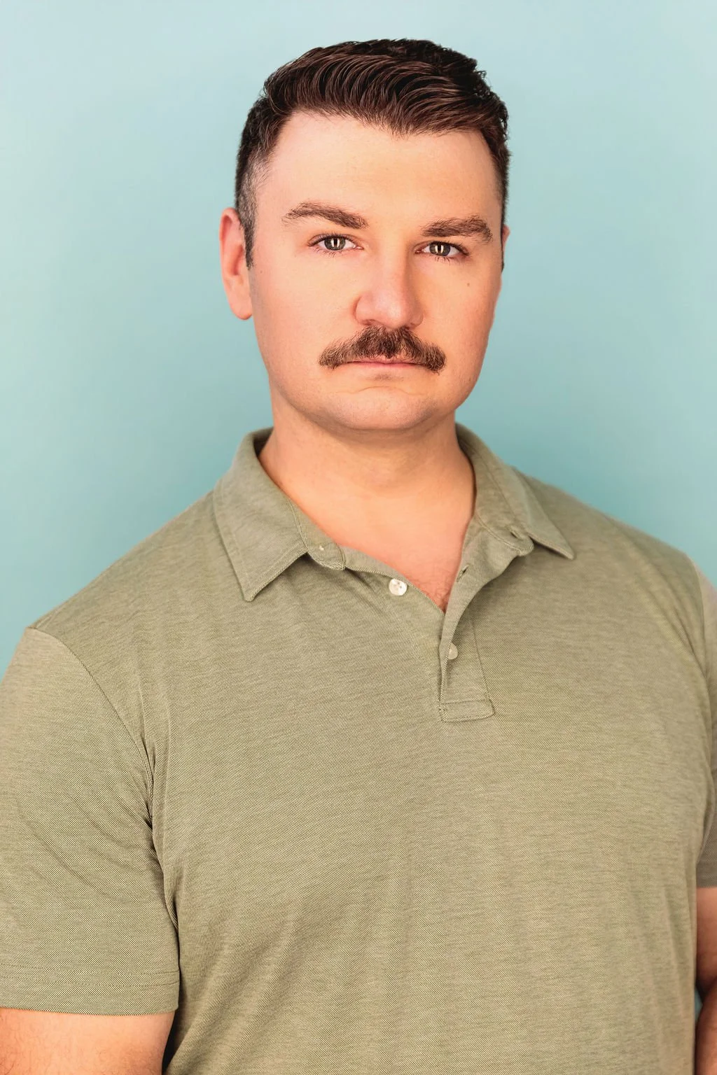 Chris Gallerani - Tenor, in a green polo against a blue background. Headshot by Benjamin Rose Photography.