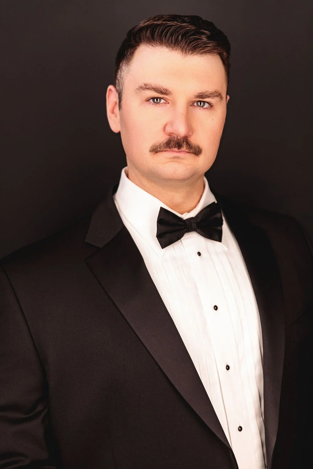 Chris Gallerani - Tenor, in a tuxedo with a black bow tie and a white dress shirt against a dark background. Headshot by Benjamin Rose Photography.
