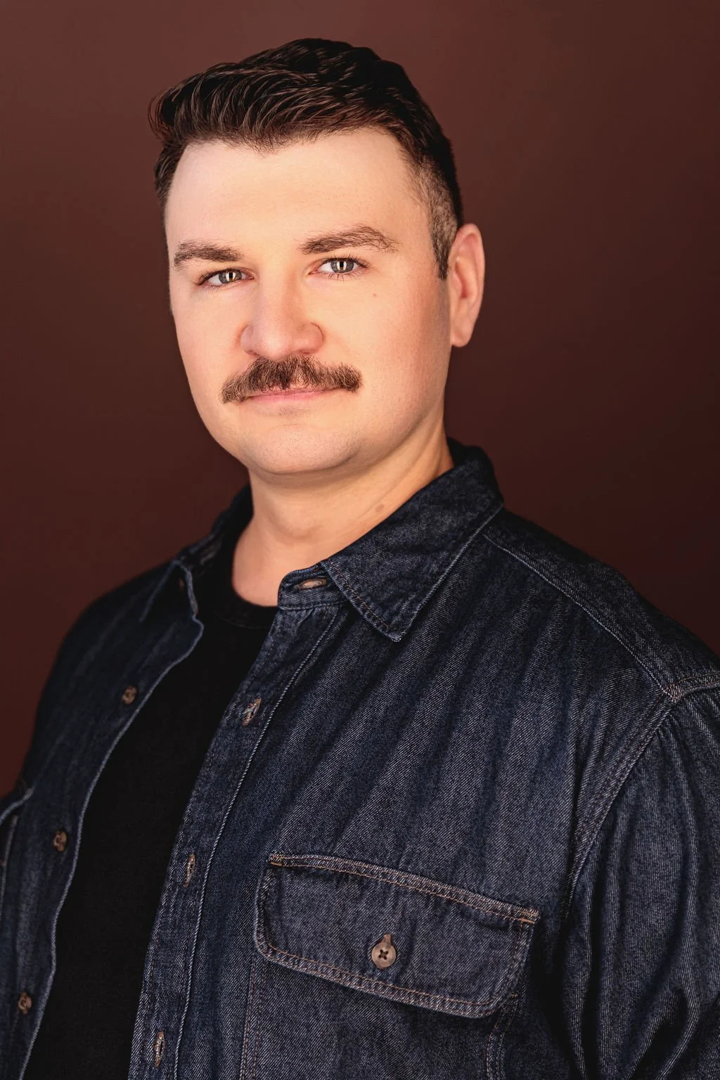 Chris Gallerani - Tenor, smiling in a denim shirt against a brown background. Headshot by Benjamin Rose Photography.