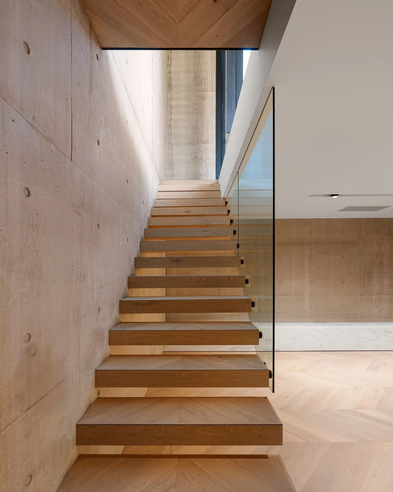 Modern interior with light wood staircase, concrete floor, and white wall ceiling.