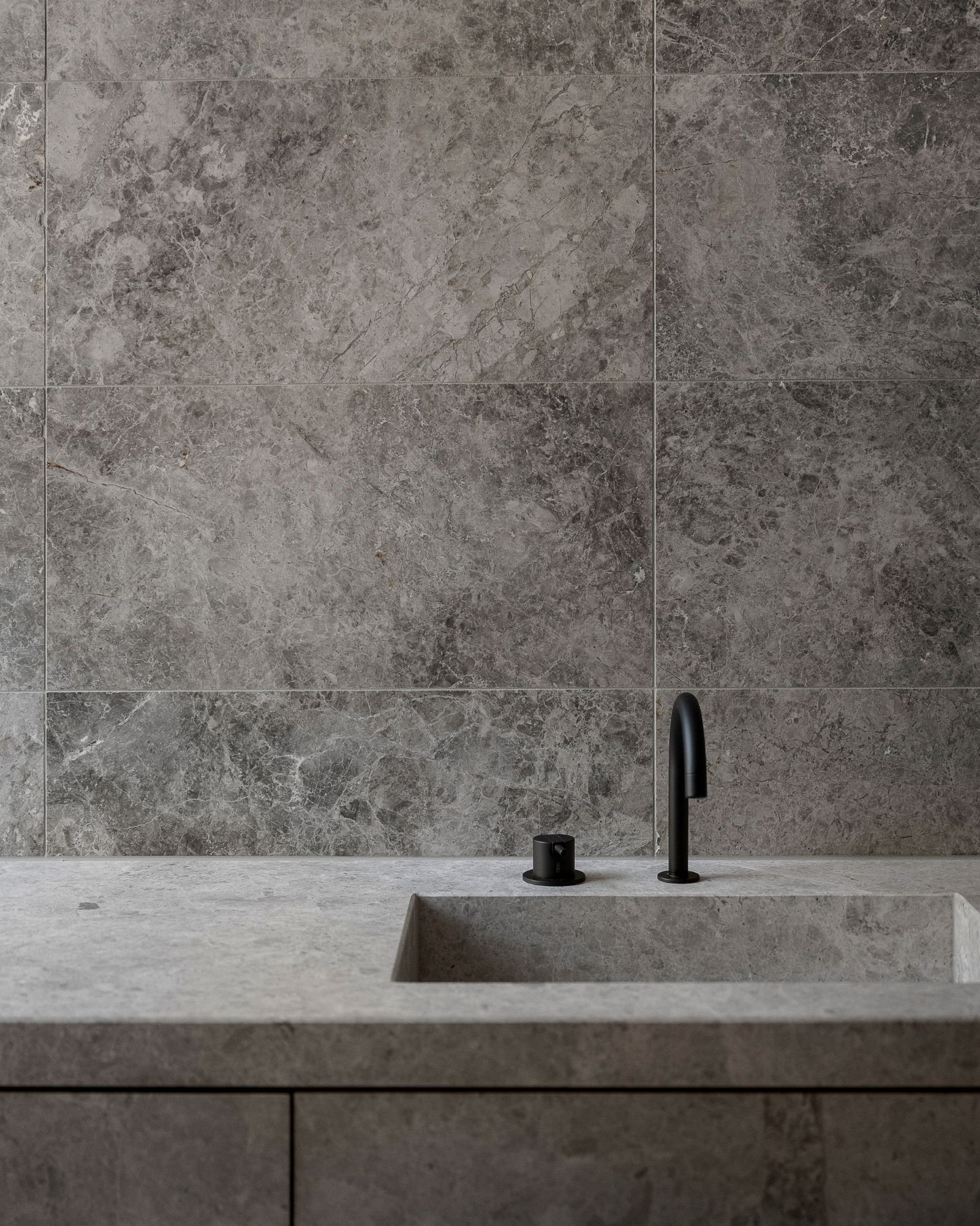 A modern kitchen countertop with a black faucet and sink, gray stone backsplash, and minimalist design.