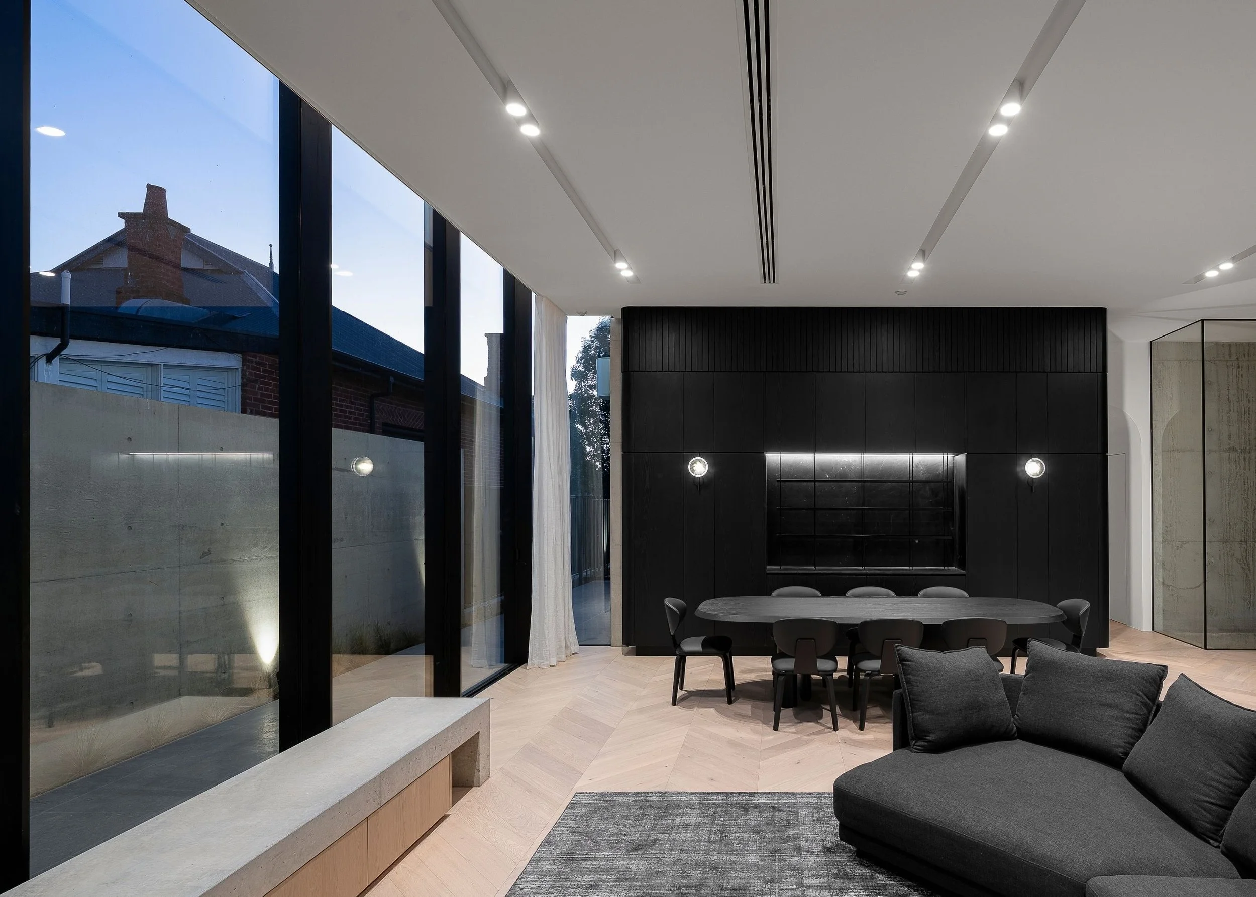 Modern interior living space with large floor-to-ceiling windows, black built-in cabinets, dining table with chairs, and gray sofa.