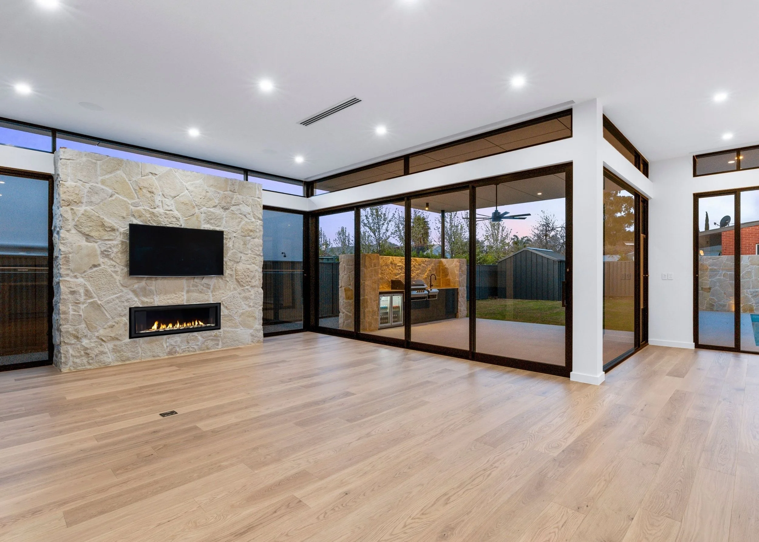 Modern living room with a stone fireplace, TV, large sliding glass doors, and wood flooring.