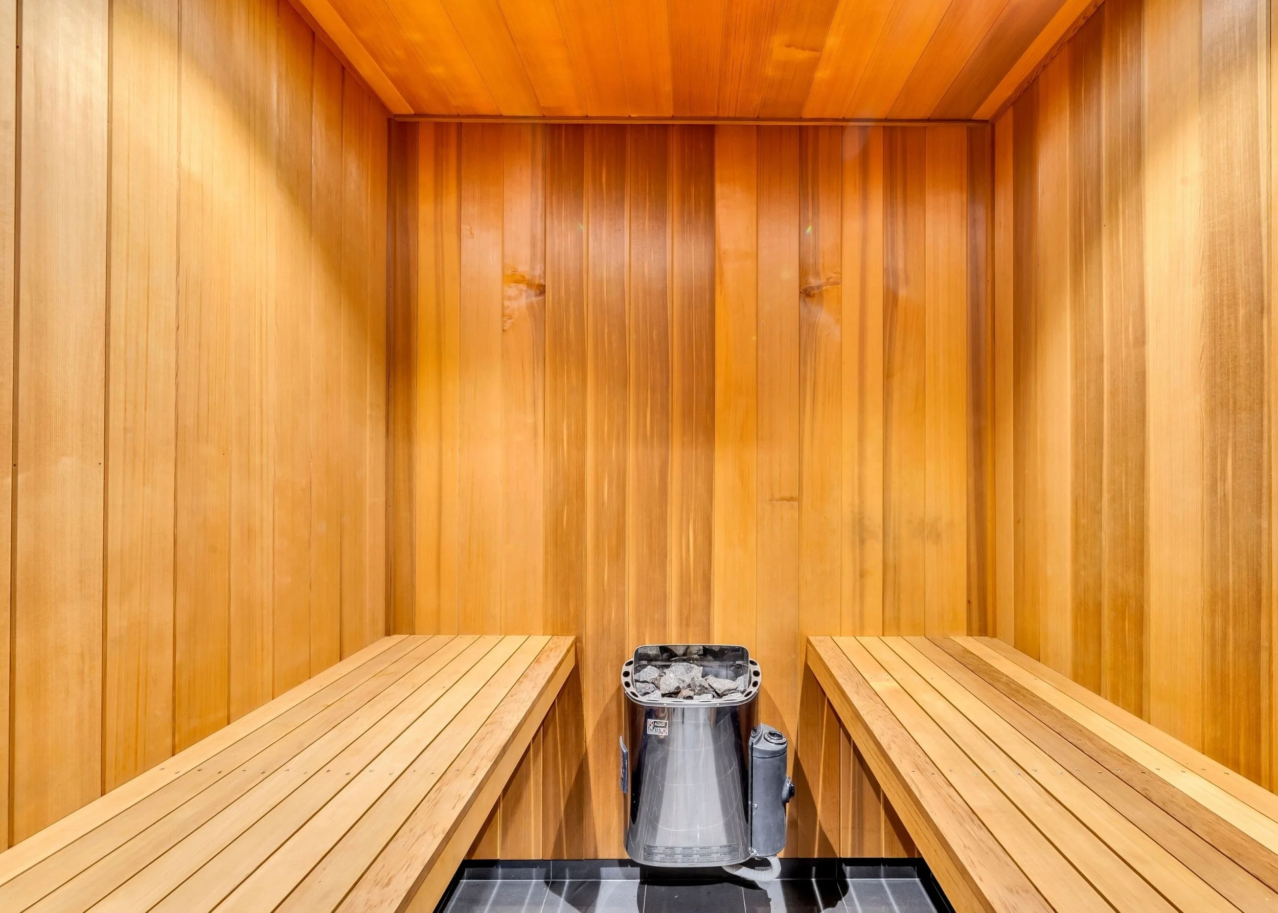 Interior of a traditional Japanese sauna with wooden walls, benches, and a heater with stones in the center.