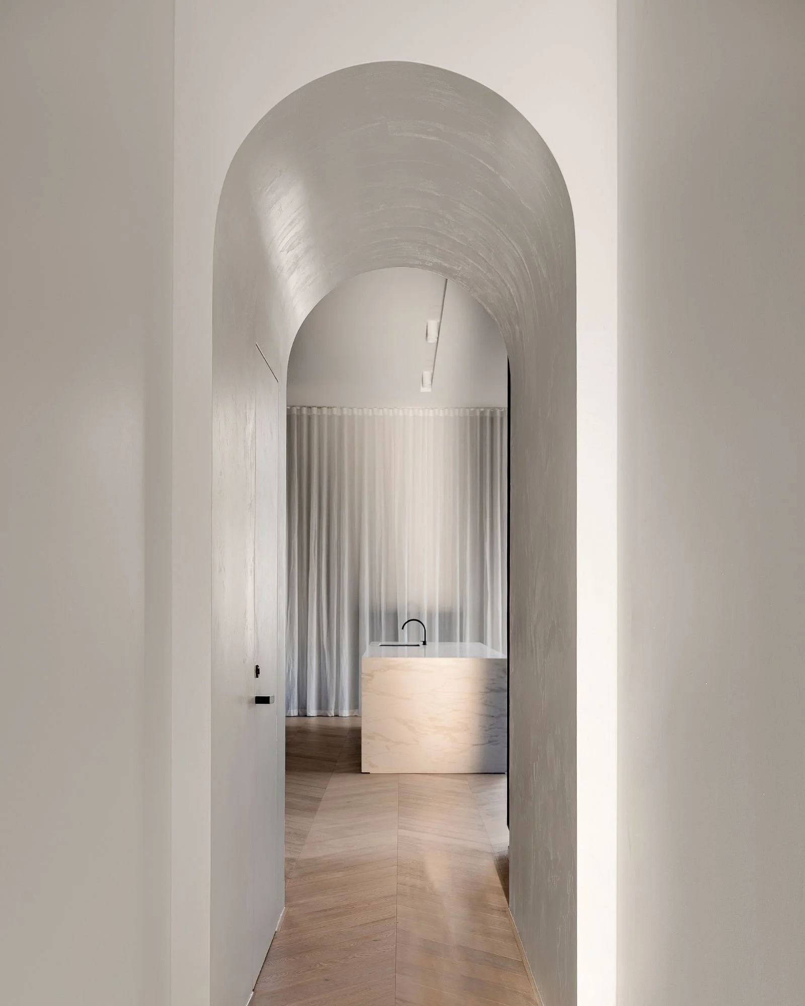 A minimalist corridor with white walls and a vaulted ceiling, leading to a space with a curtain and a marble desk or counter.