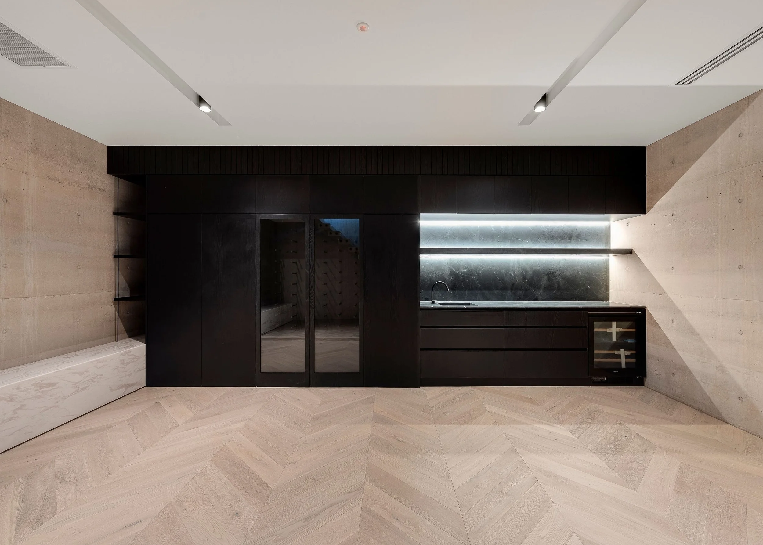 Modern kitchen with black cabinetry, marble backsplash, and light wood chevron floor. The ceiling features recessed lighting and a smoke detector.