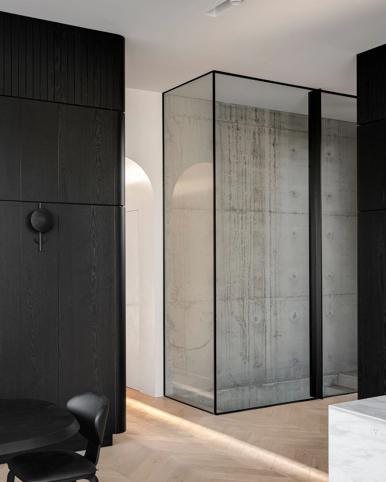 Modern interior with black cabinetry, a frosted glass partition with a black frame, a white marble table, and light wooden flooring.