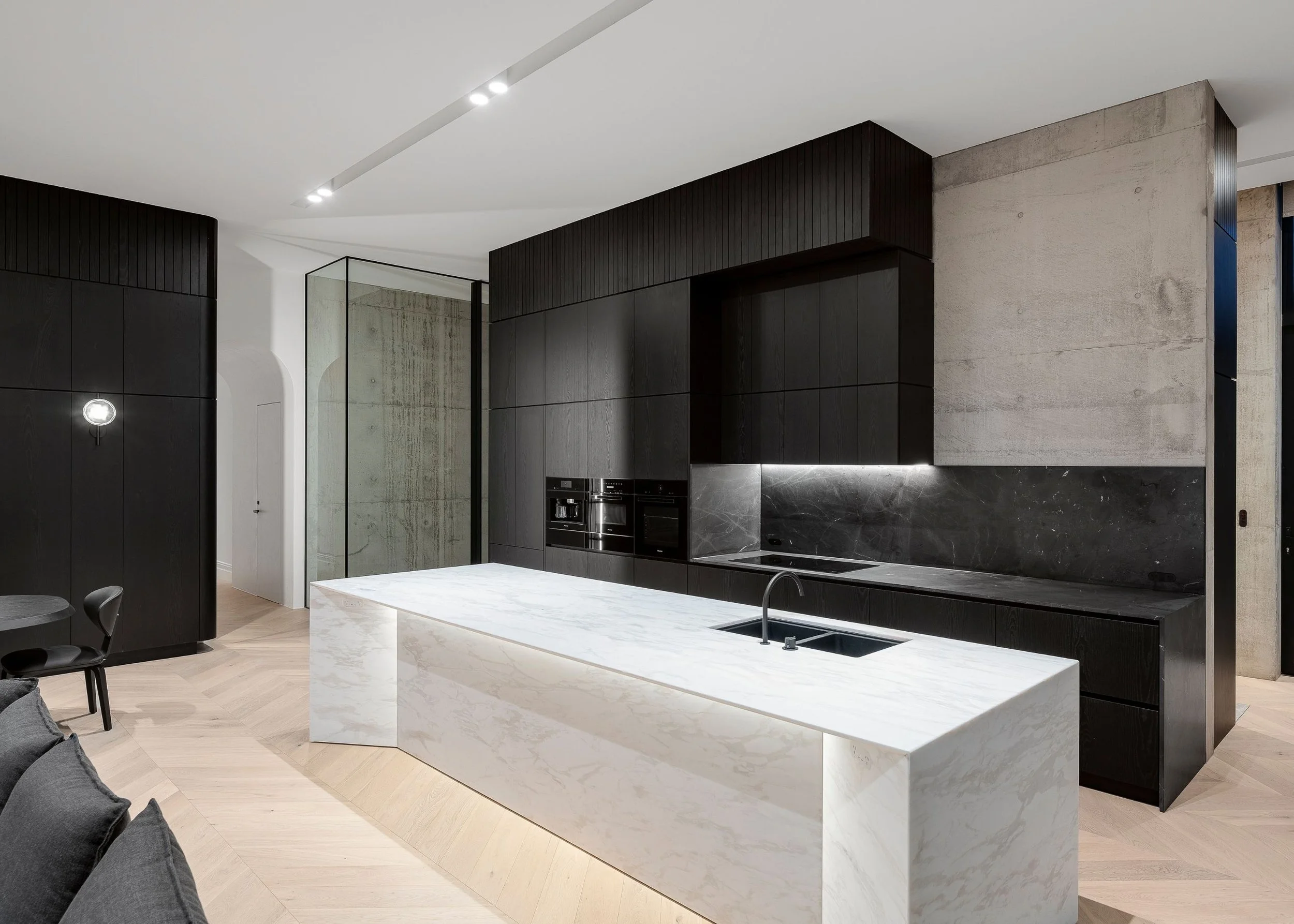 Modern kitchen with black cabinets, a marble island, and concrete wall accents in a minimalist interior design.