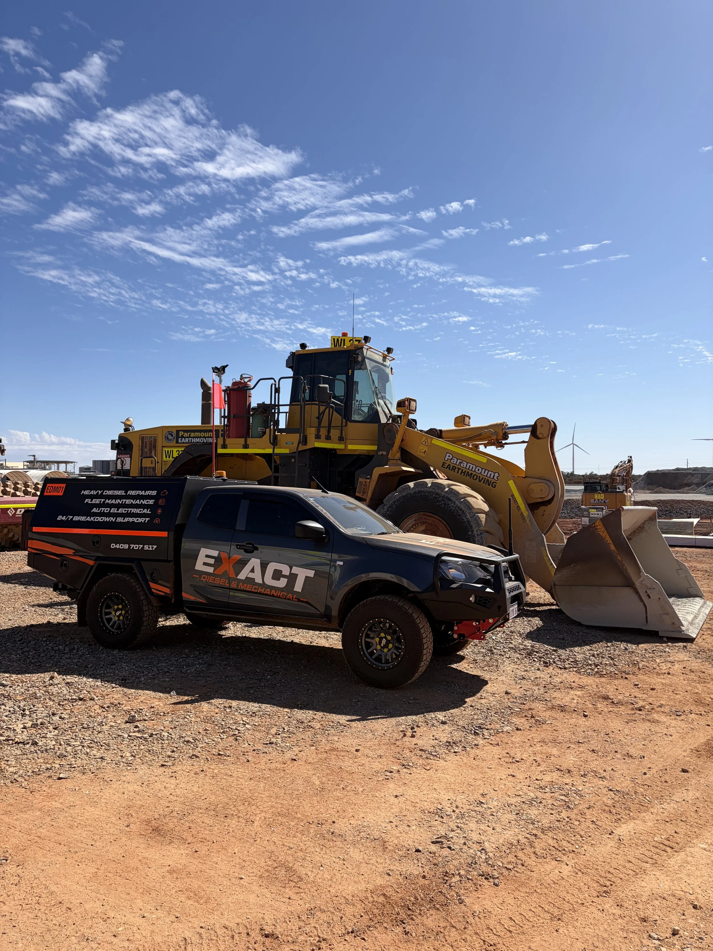 Heavy earthmoving equipment and a diesel service truck at an open-pit mining site under a blue sky