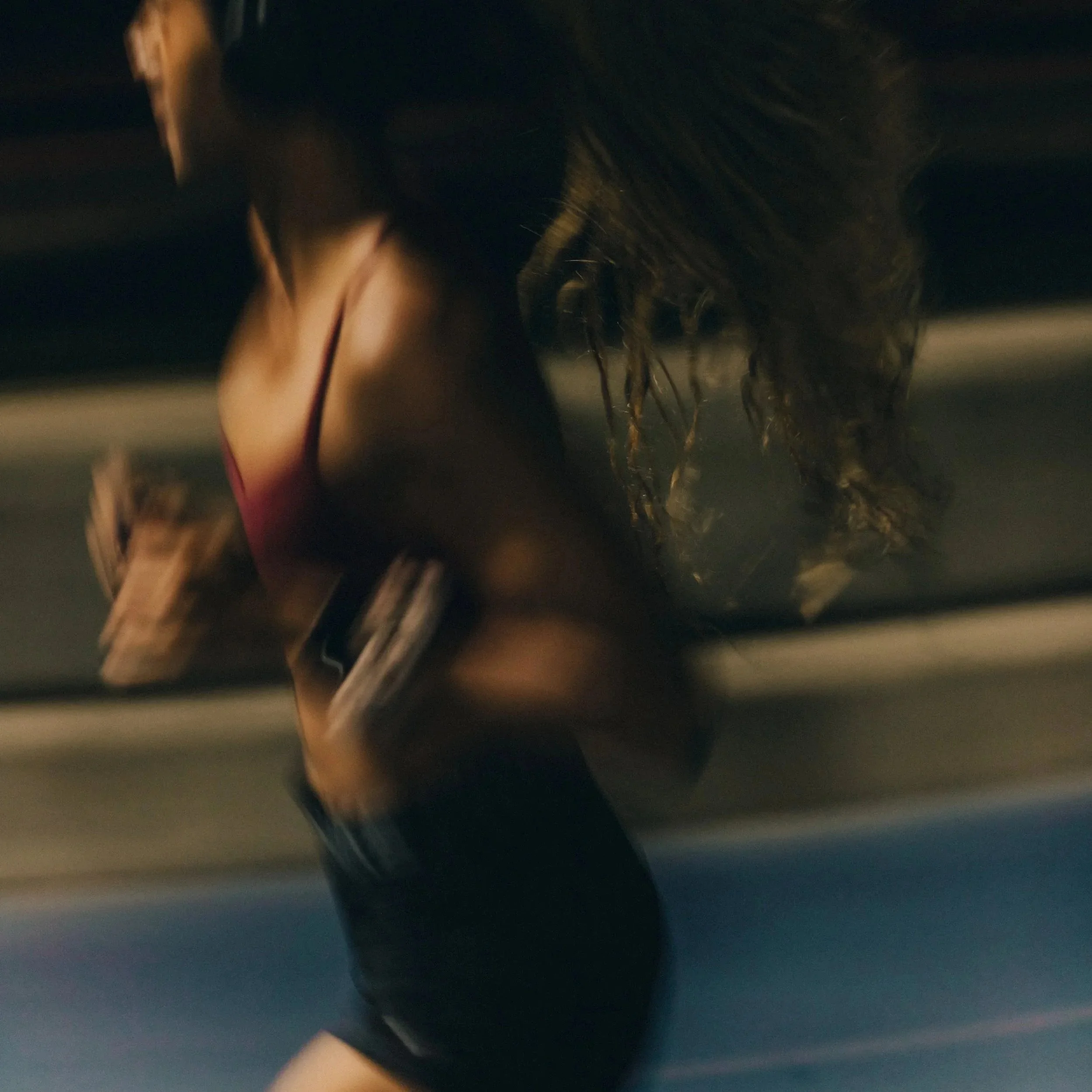 Blurred close-up of a person with long dark hair and outstretched arms running at night.