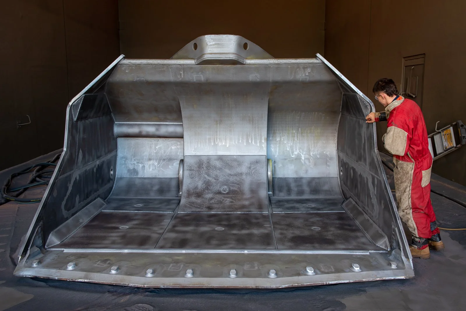Industrial worker inspecting a newly fabricated steel scoop inside a manufacturing workshop