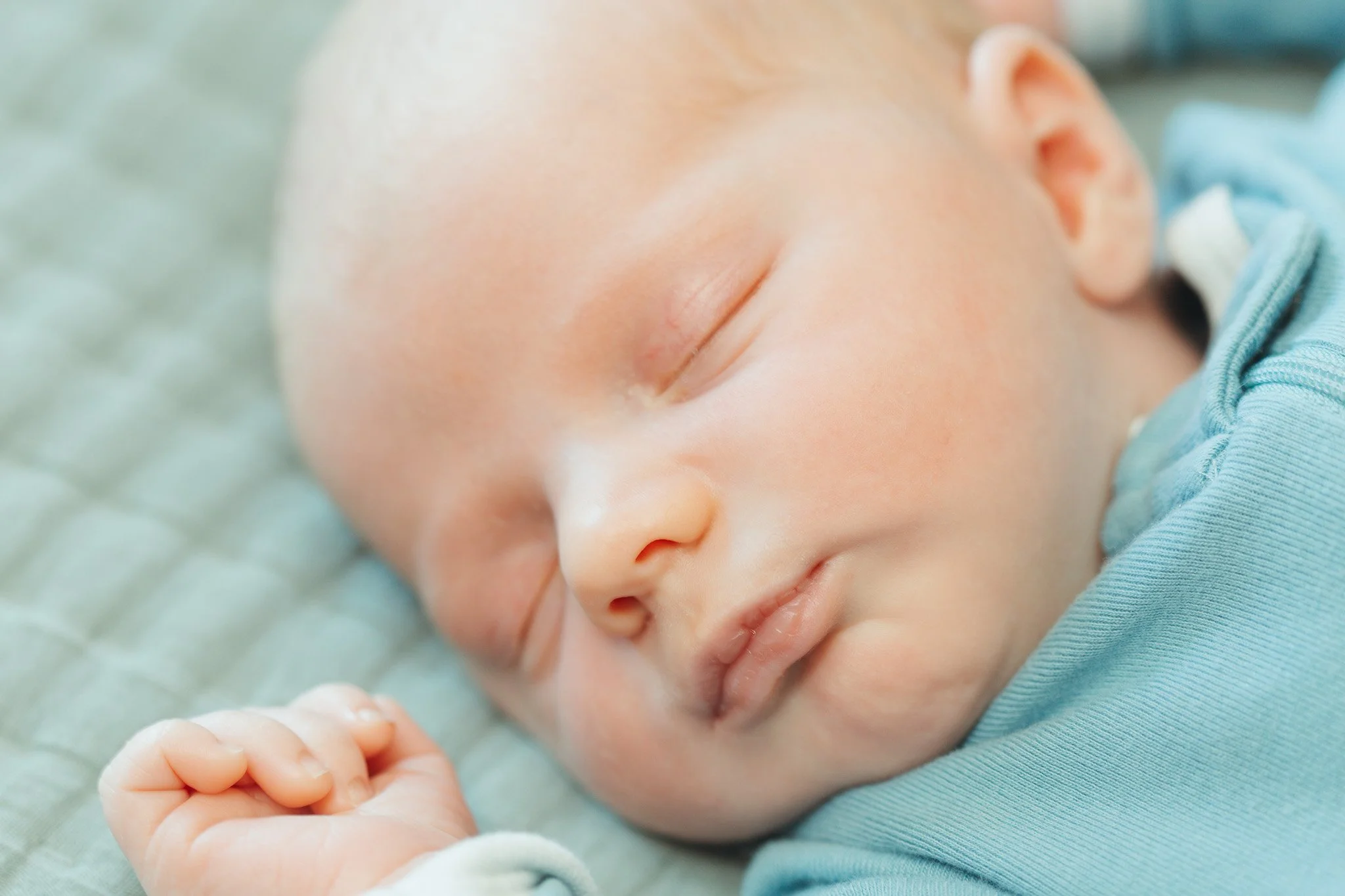 Close-up of a sleeping newborn baby lying on its side with eyes closed, resting peacefully.