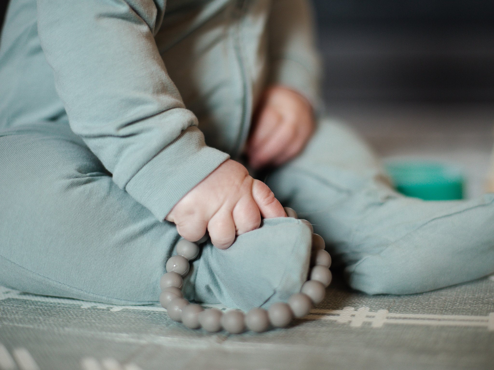 Close-up of a person's crossed arms, wearing a light gray hoodie, with a beige beaded bracelet resting on the person's arms.