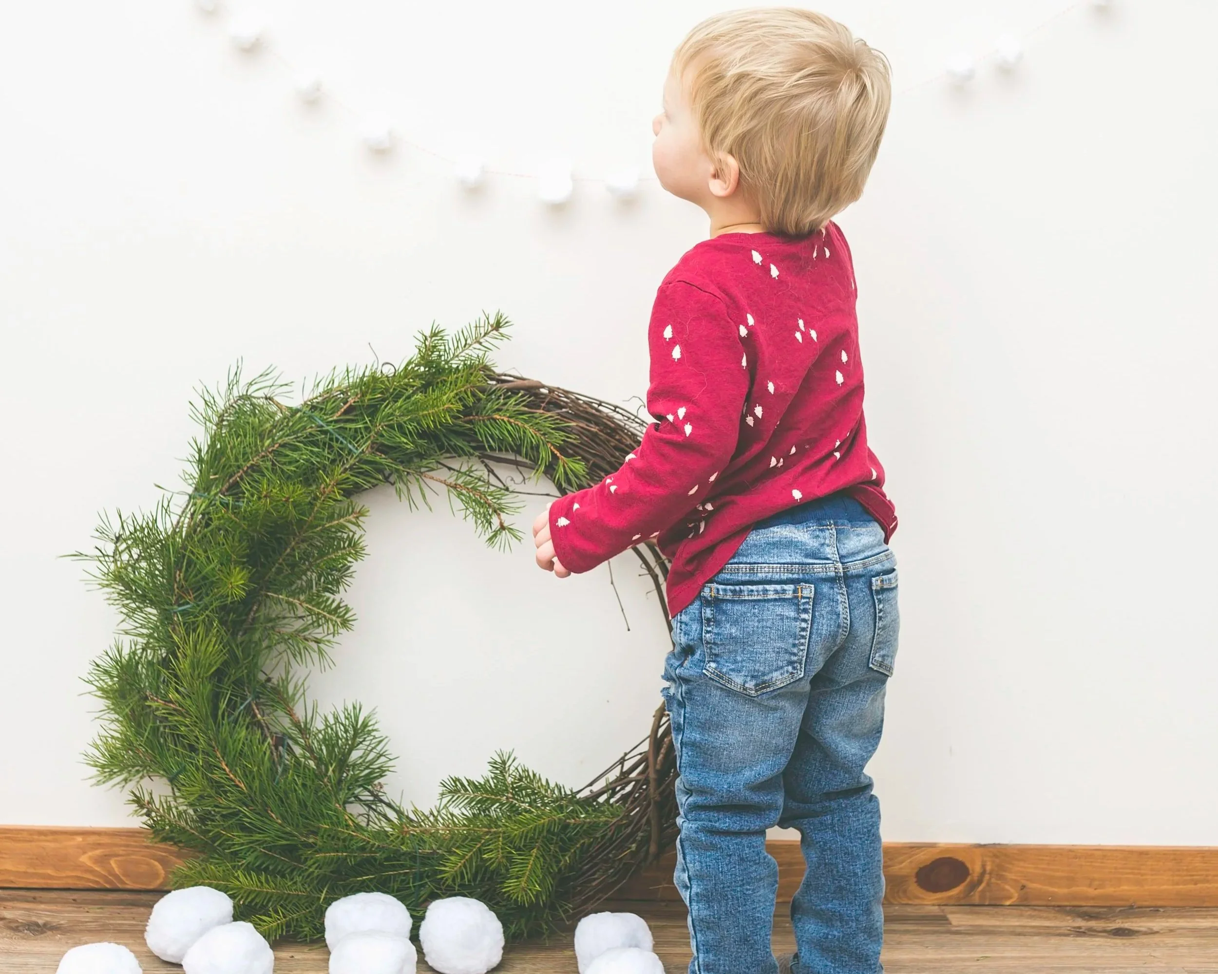toddler boy looking at holiday Christmas decorations wreath on wall