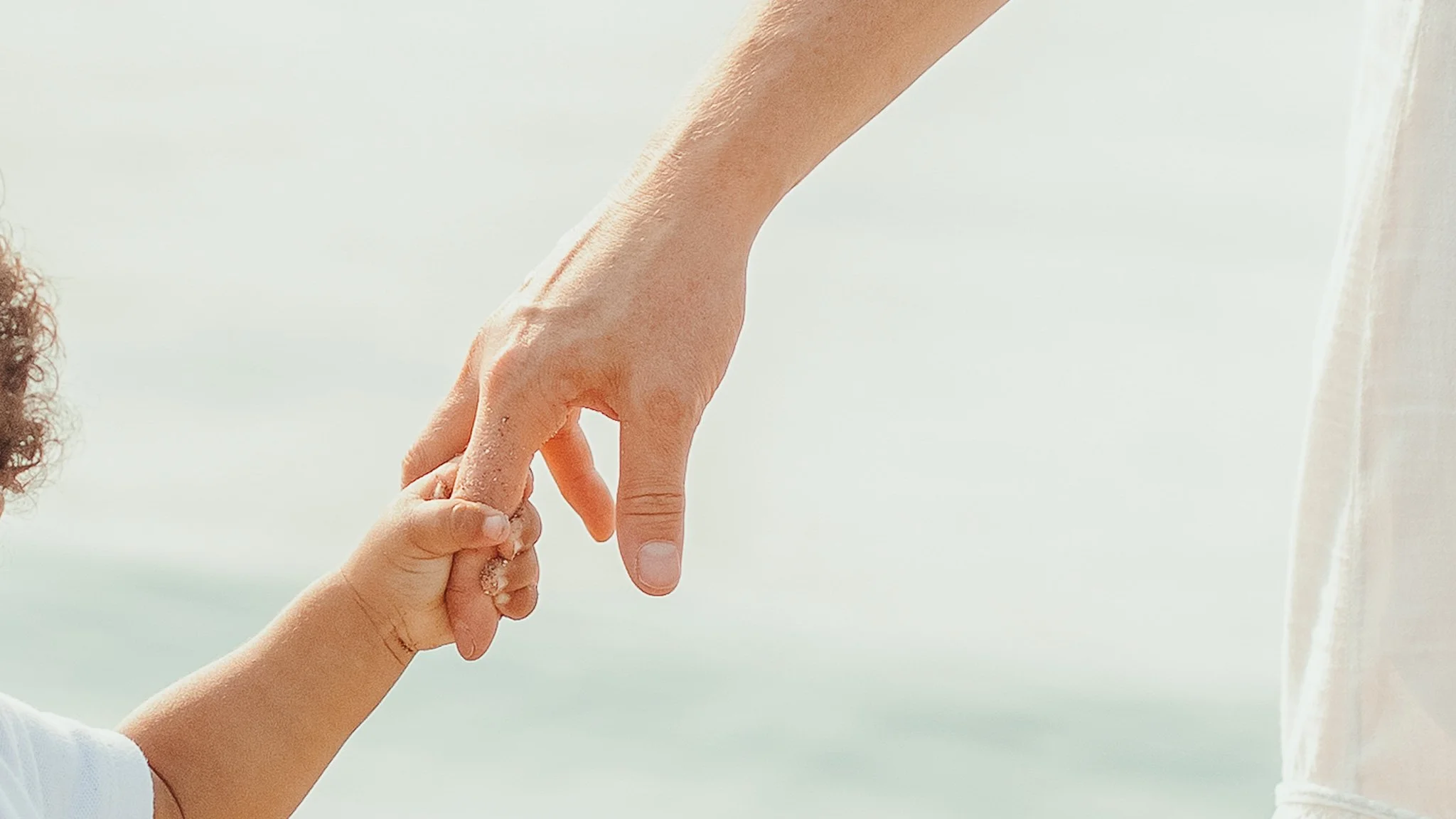 A child's hand holding an adult's index finger, both hands appear to be touching or connecting.