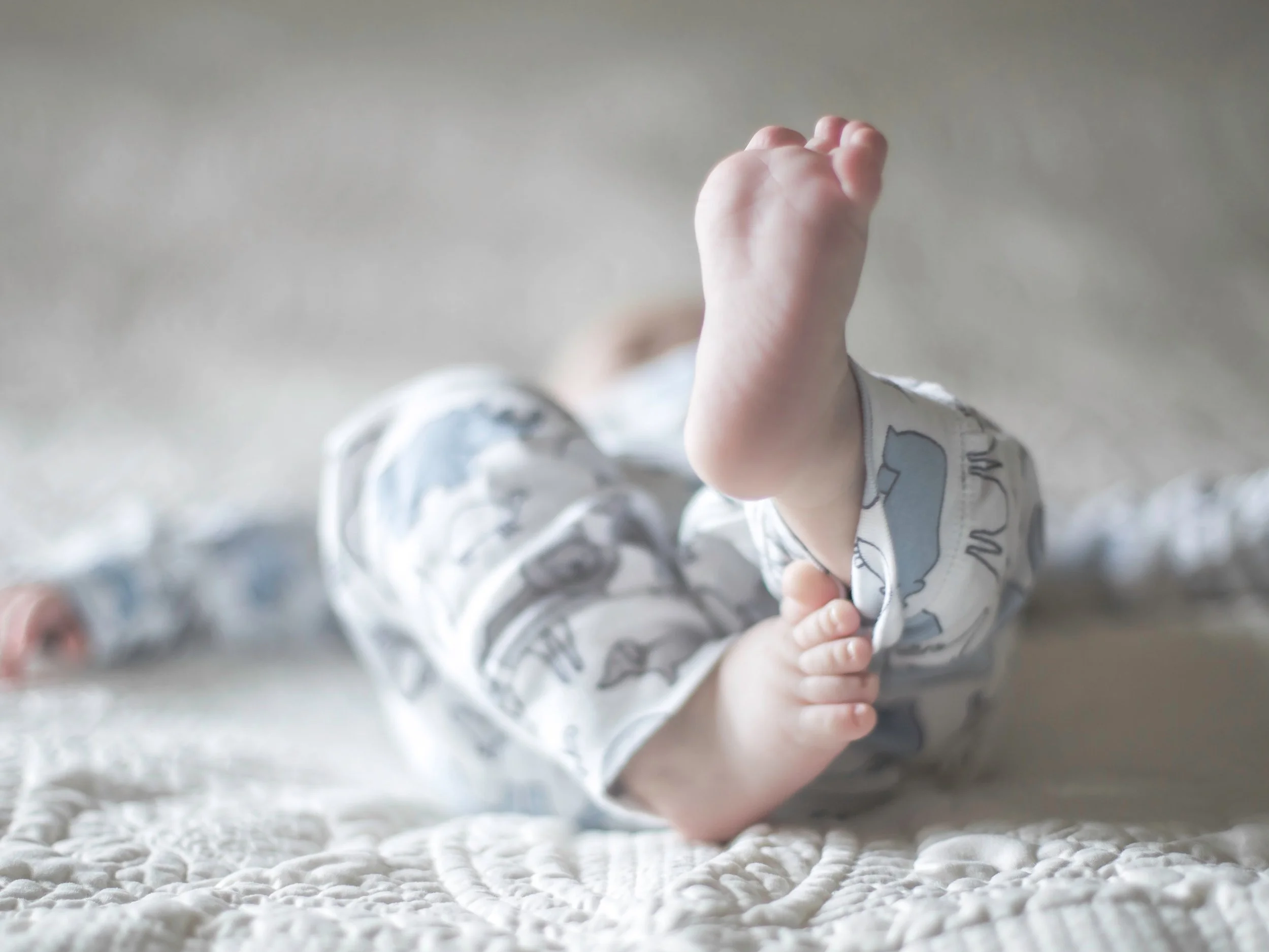 Close-up of a baby lying on a soft, textured surface, with an arm raised and hand clenched into a fist.