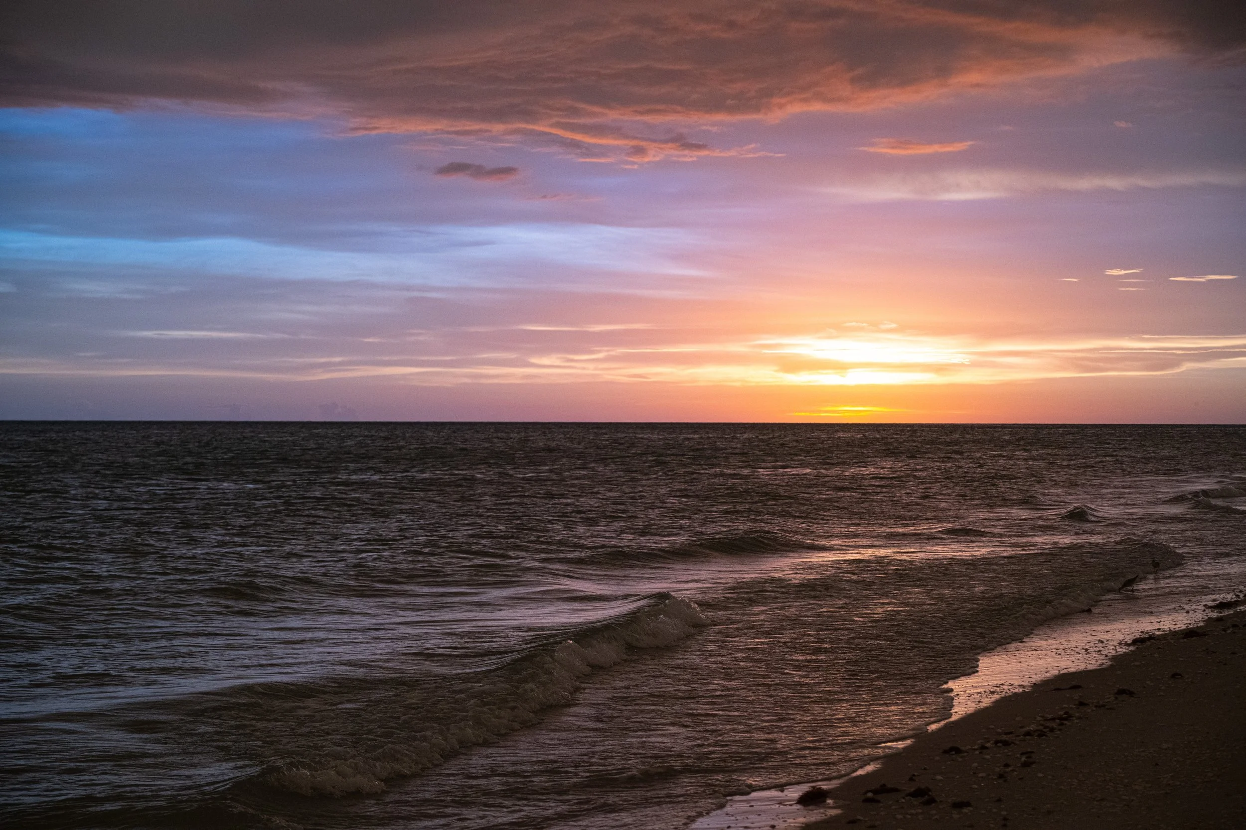 Sunset over the ocean with a colorful sky of pink, purple, and orange hues, and gentle waves lapping at the sandy shore.