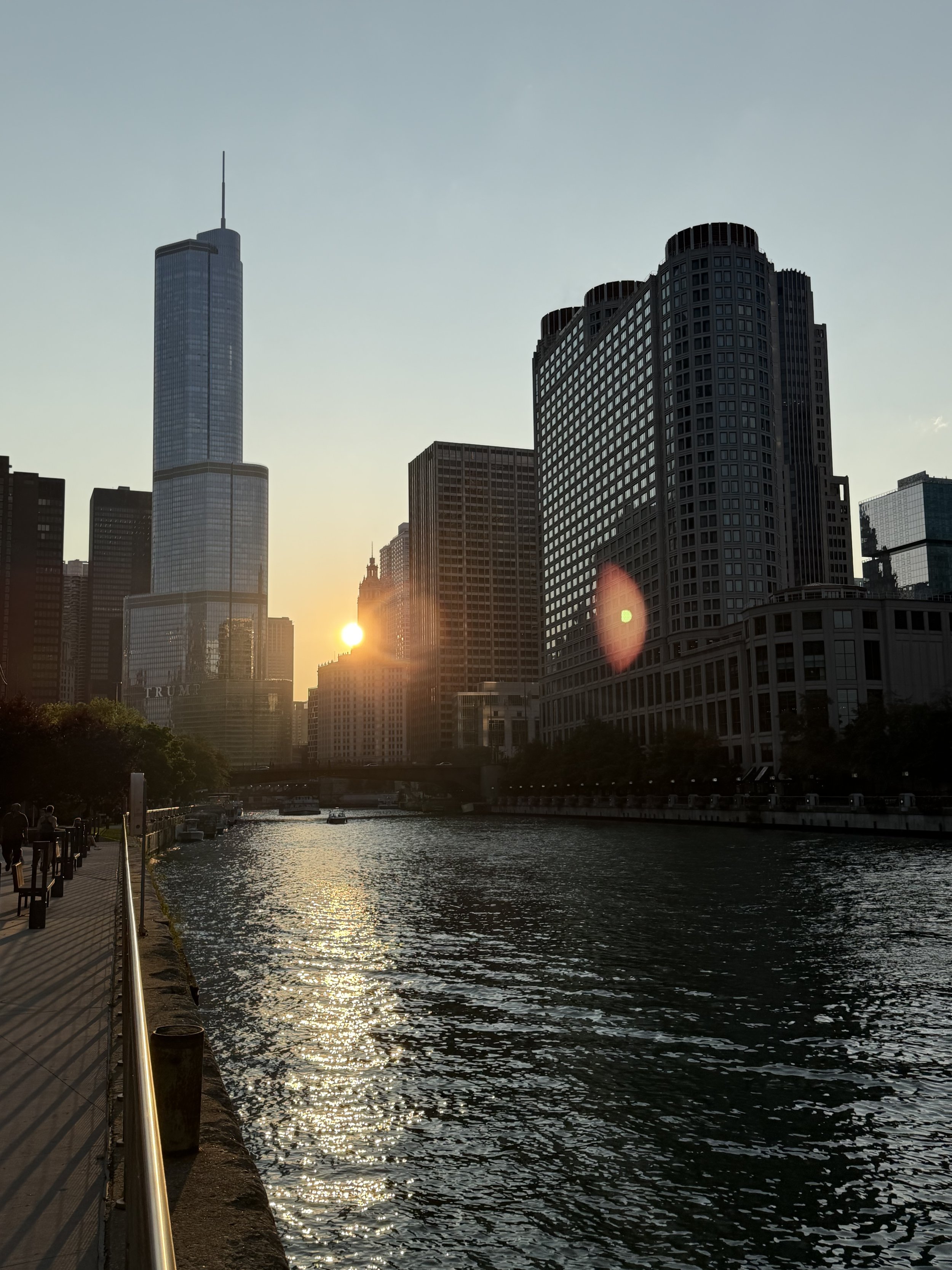 City skyline at sunset with tall buildings and a river in the foreground