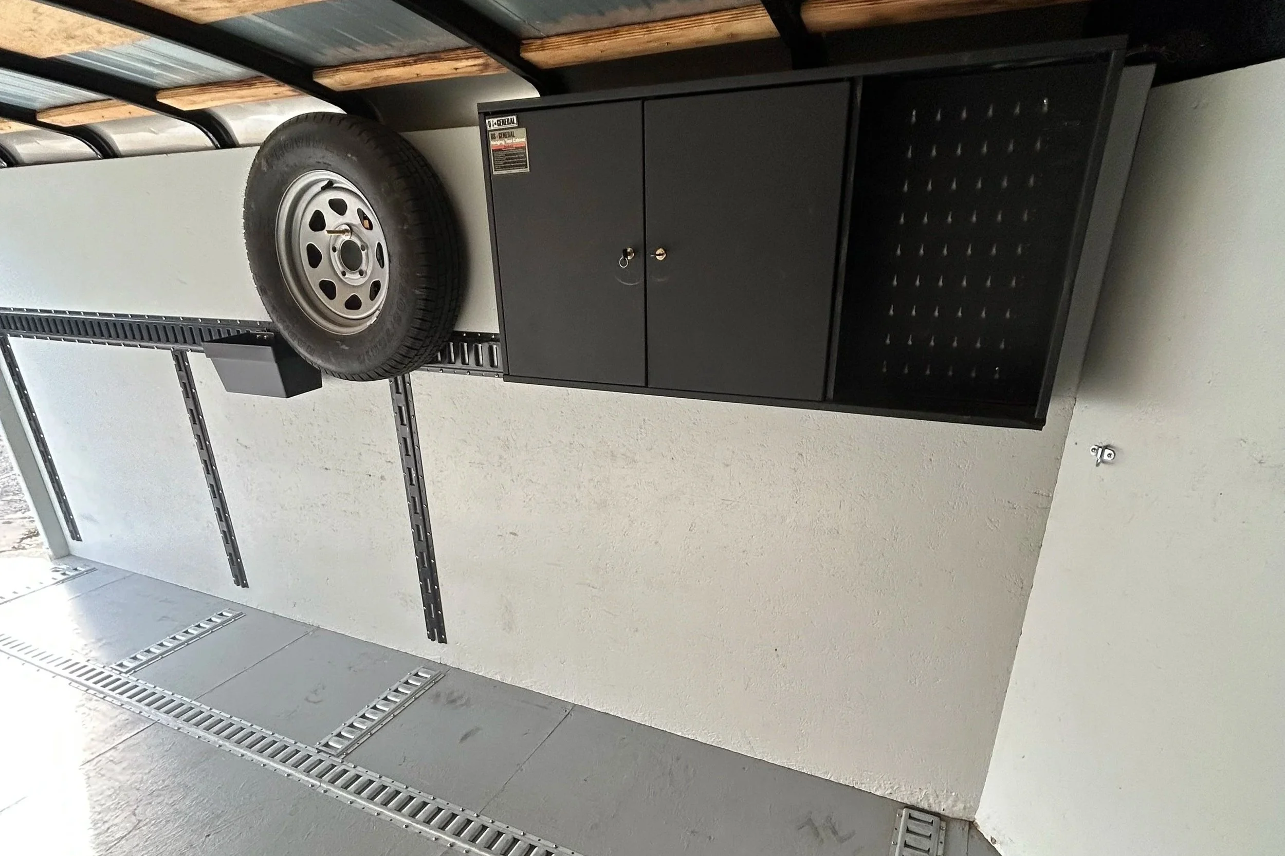 A garage storage area with a black metal tool cabinet, wheel, and shelving.