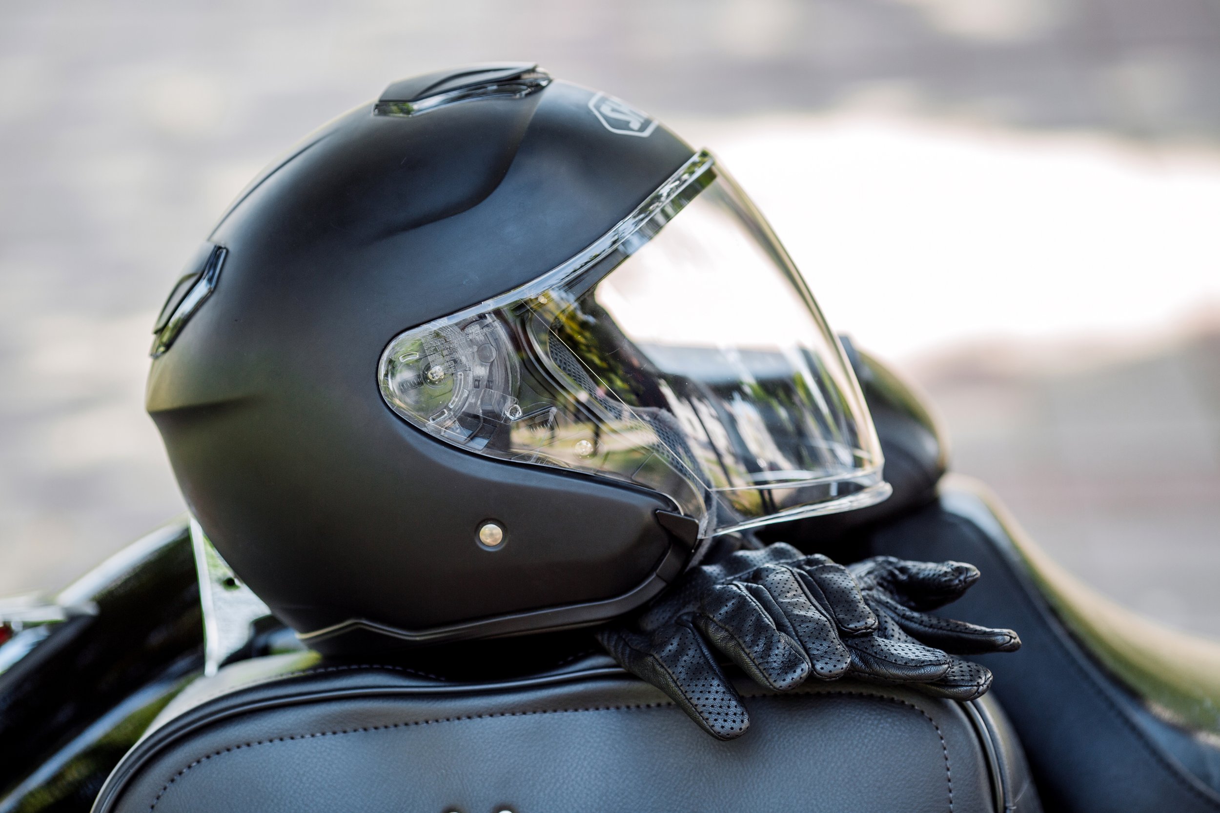 Motorcycle helmet resting on a motorcycle seat, with black gloves underneath, outdoors with soft sunlight.