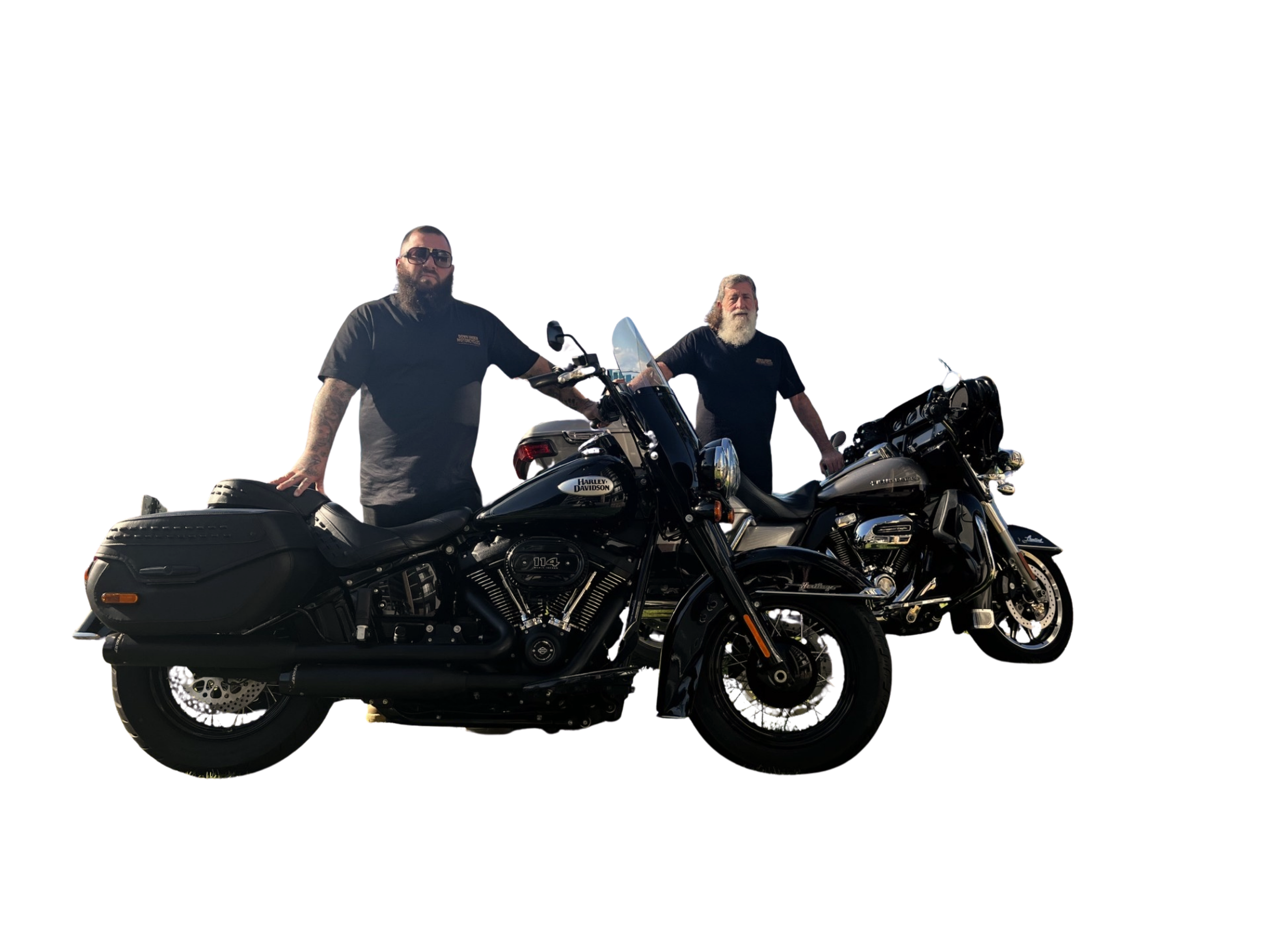 Two men standing beside black Harley Davidson motorcycles, wearing black shirts, one with sunglasses and the other with long white hair and a beard, in an outdoor setting.