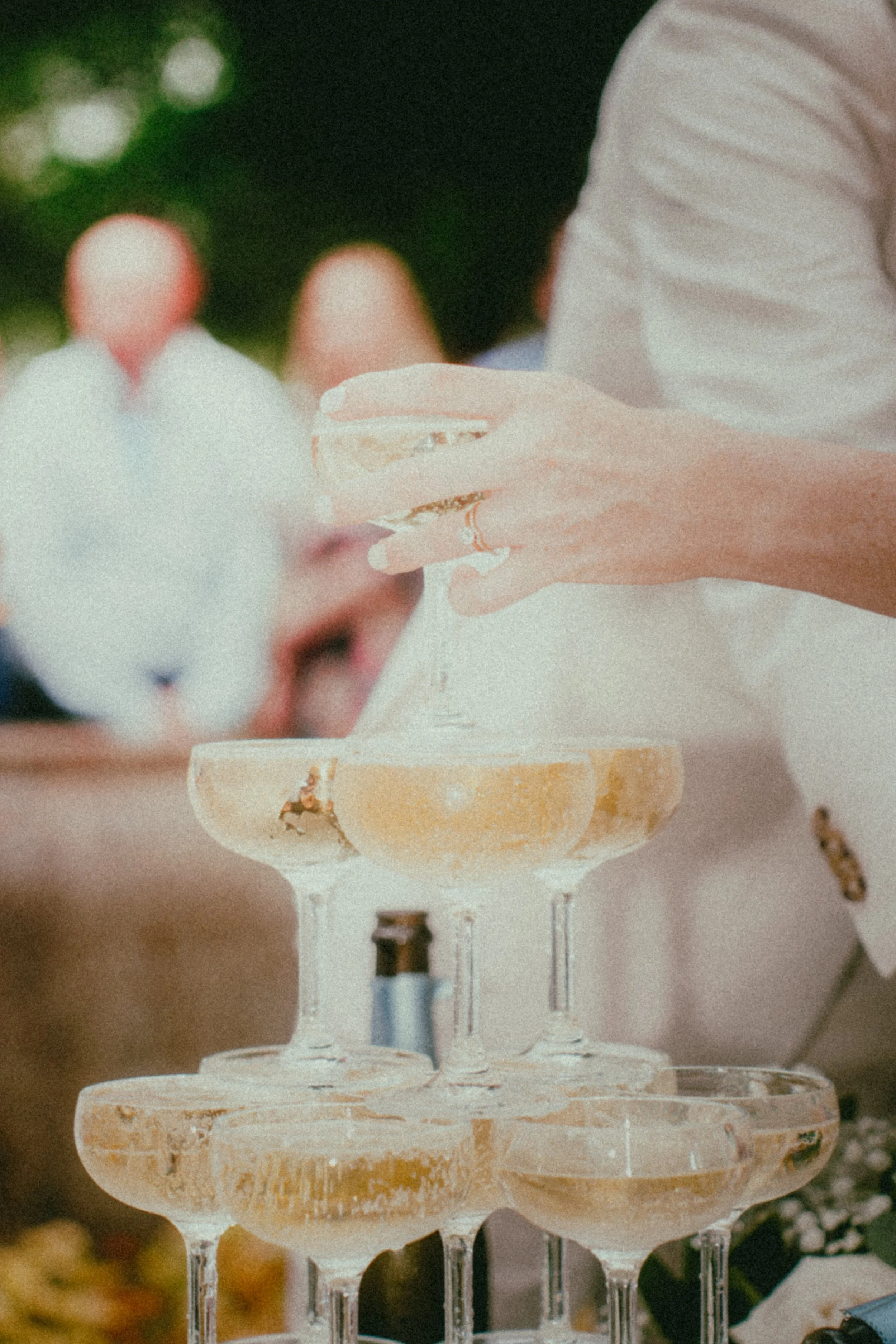 Multiple tiers of empty, chipped champagne glasses arranged in a pyramid at a celebration or wedding.