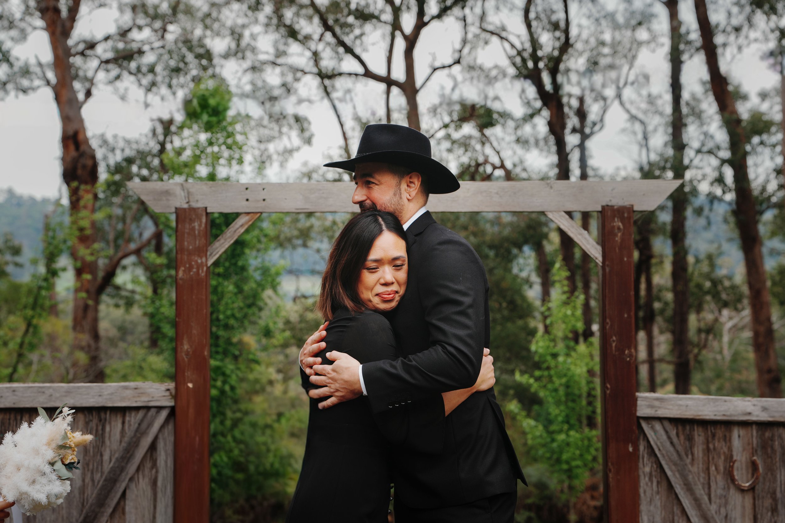 A man and woman hugging outdoors with trees in the background