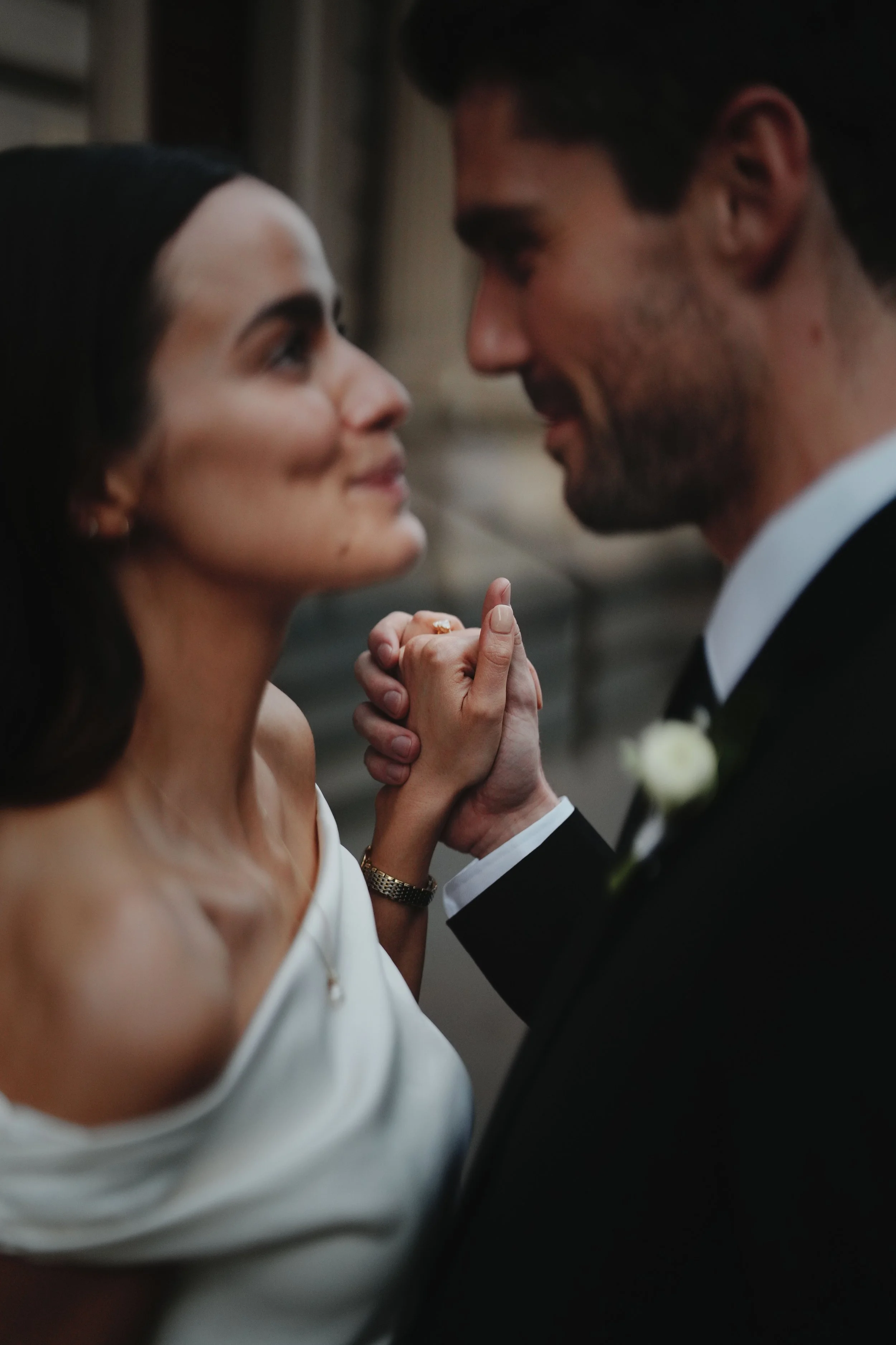 A close-up of a bride and groom facing each other, holding hands, smiling, and about to kiss during a wedding ceremony.