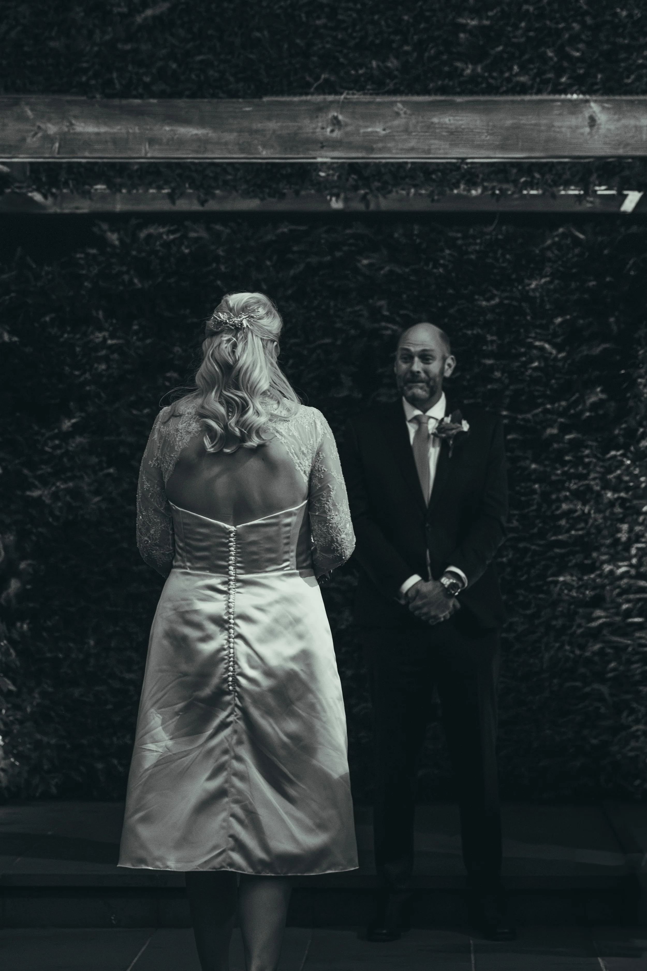 A woman in a wedding dress standing in front of a mirror with a man in a suit reflected behind her.