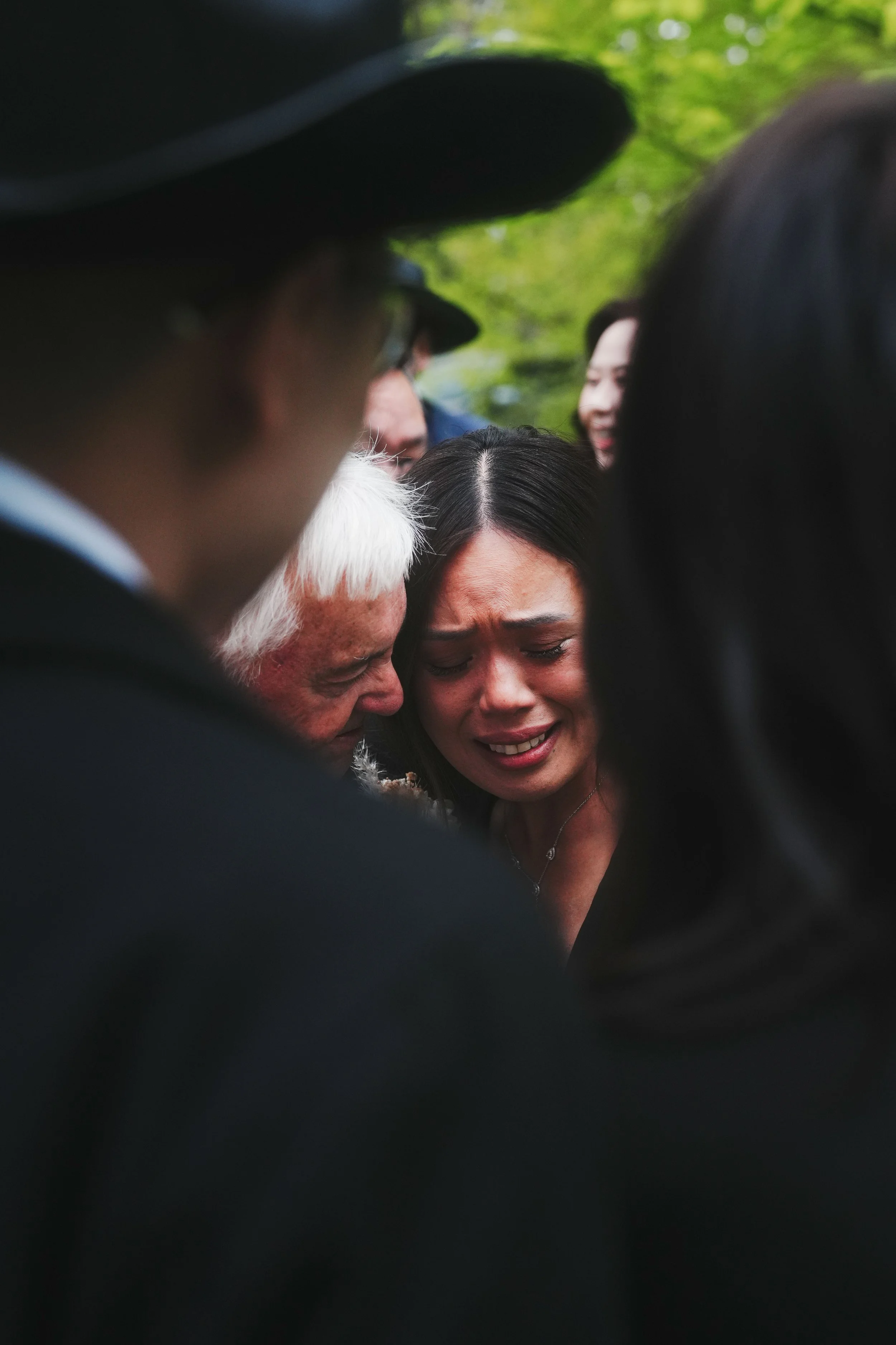 A close-up view of multiple people in a circle, showing emotions of sadness and grief, with one woman visibly crying.