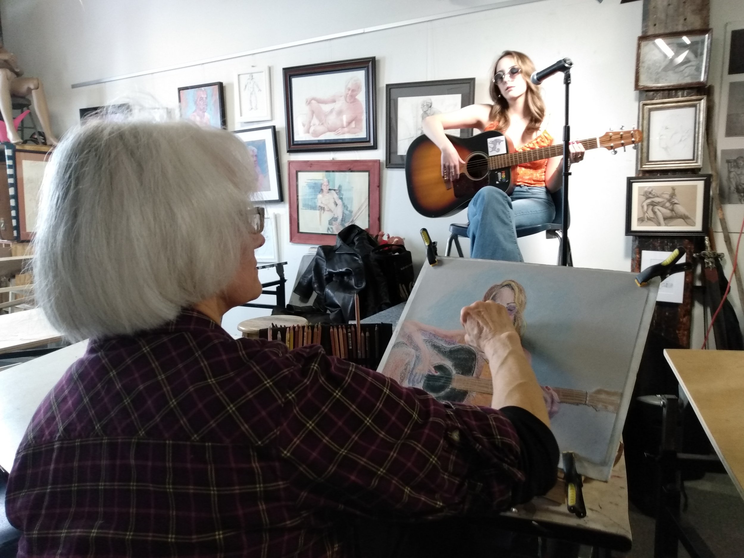Artist performing with guitar in art gallery surrounded by framed artwork.