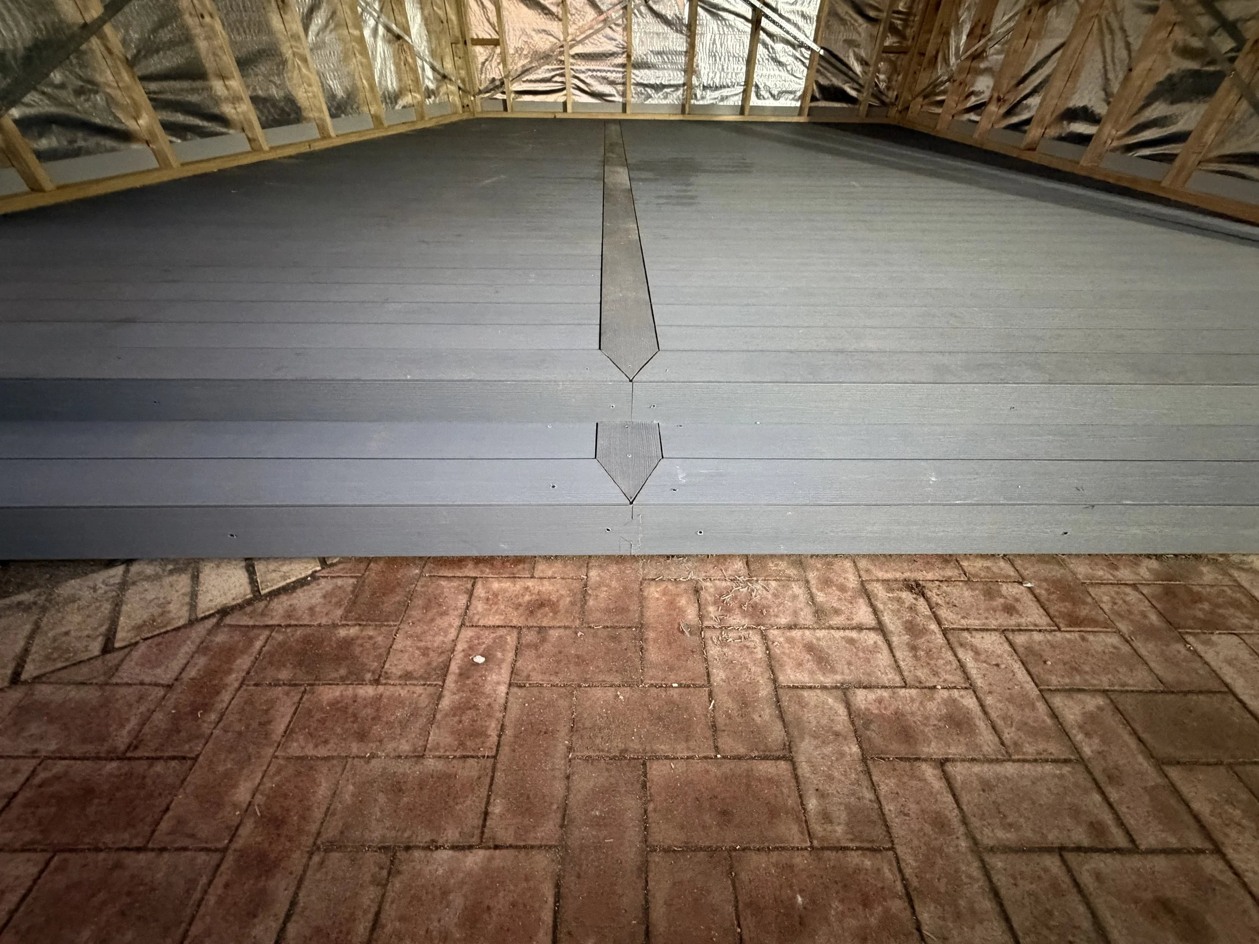 Photo of a roof under construction, with wooden framing and metal roofing panels. The roof extends over a brick patio area.