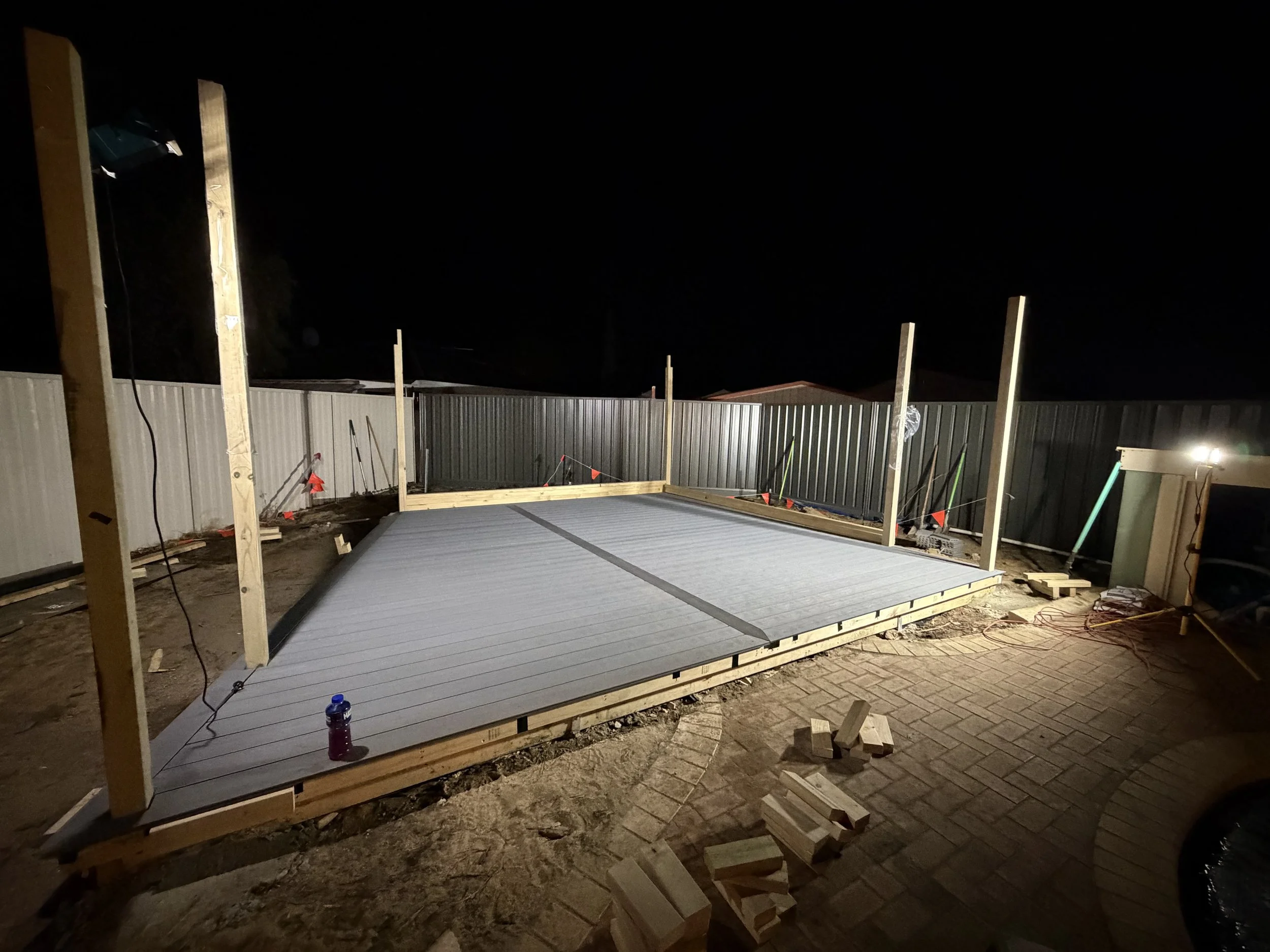 Nighttime construction site with partially built wooden structure, vertical supports, and scattered bricks and tools on the ground.