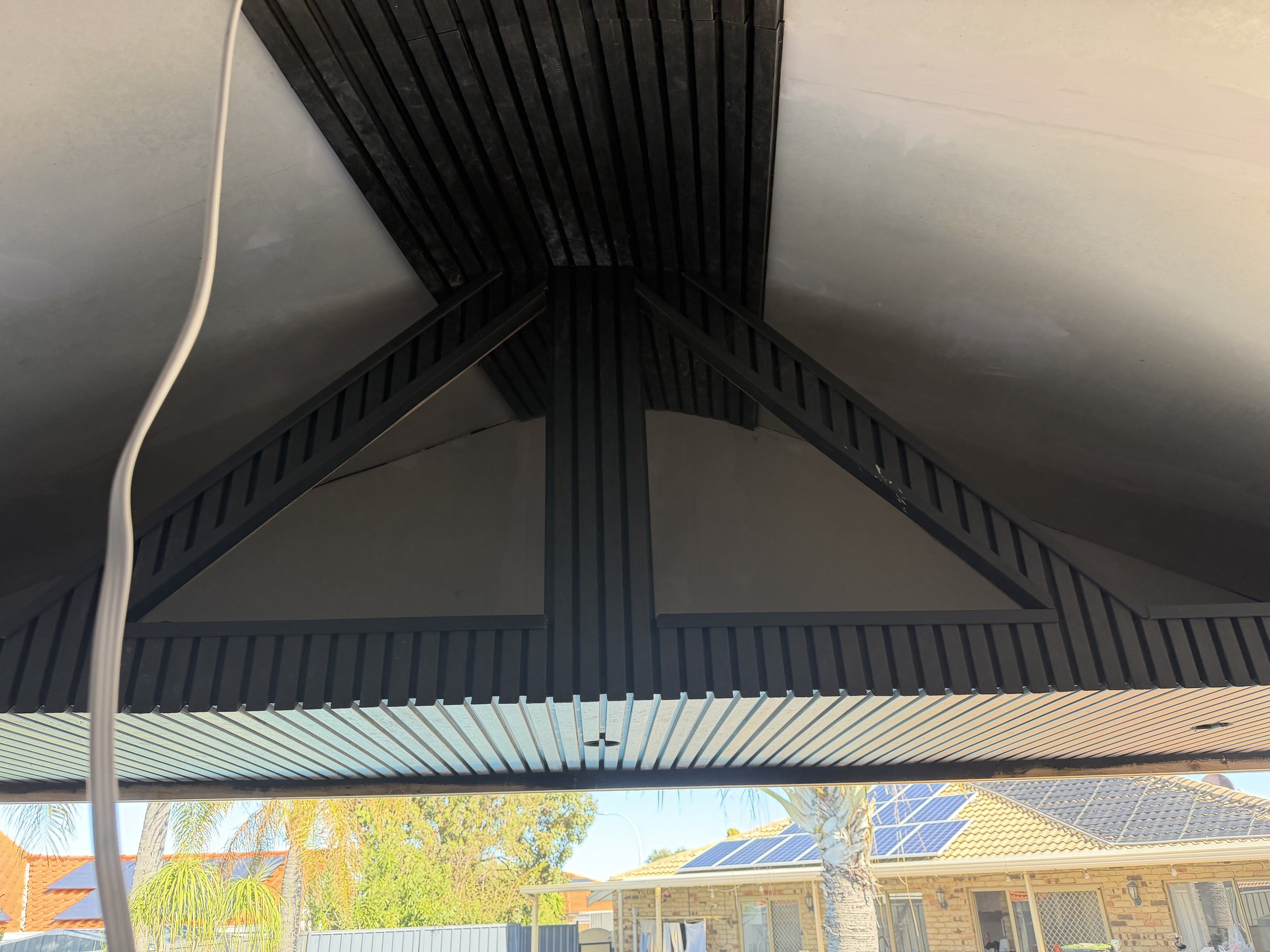 Looking up at a corner of a house roof with solar panels and trees in the background.