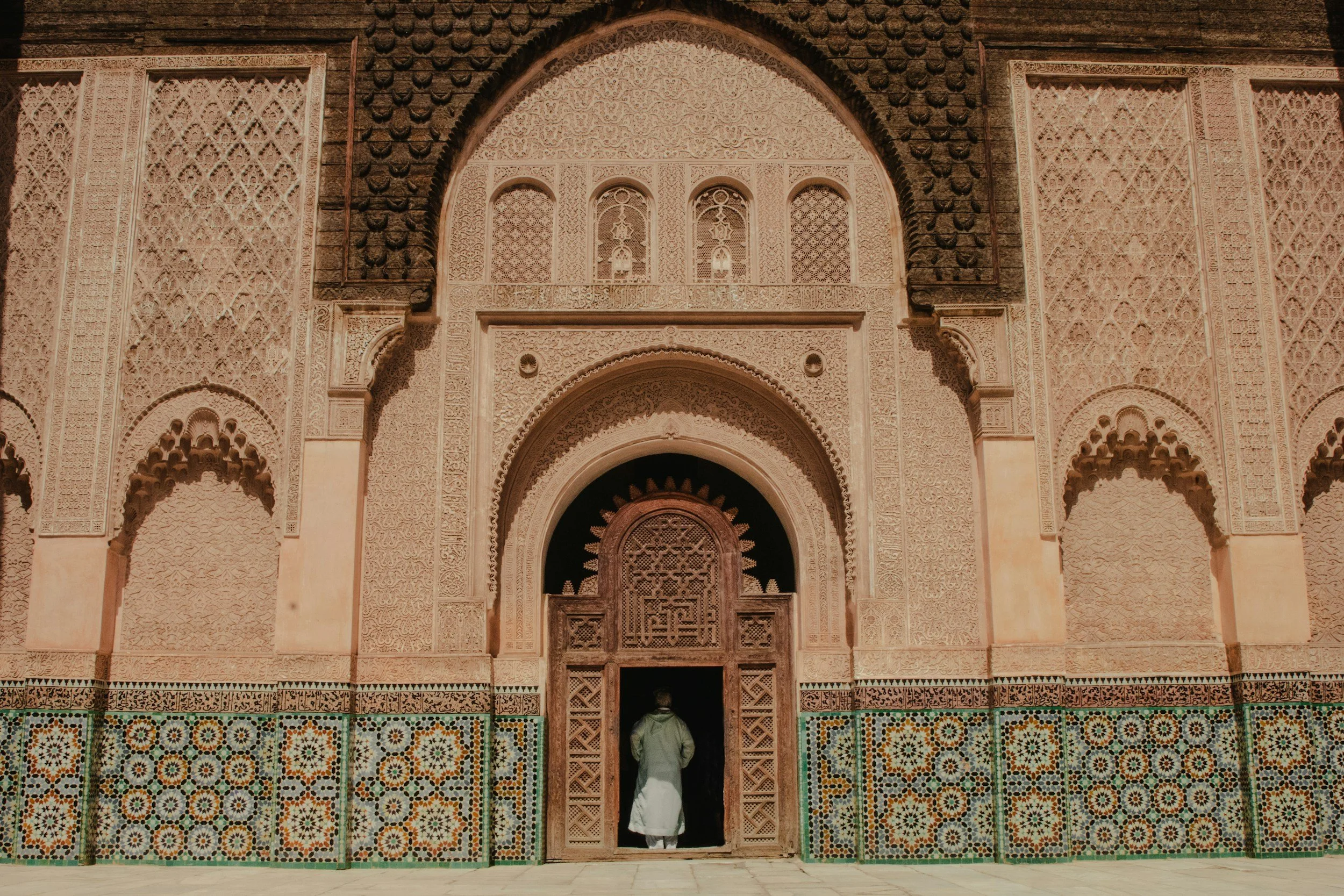 An intricately decorated building facade with detailed carvings and stained glass windows, featuring a person entering through a door at the bottom center of the image.