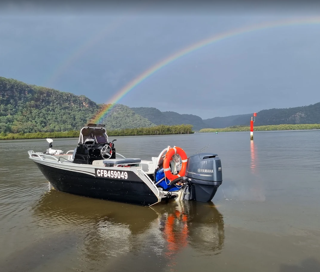 A black and white motorboat equipped with a Yamaha engine, floating on calm water with a rainbow arching across the cloudy sky in the background, and mountains visible in the distance.