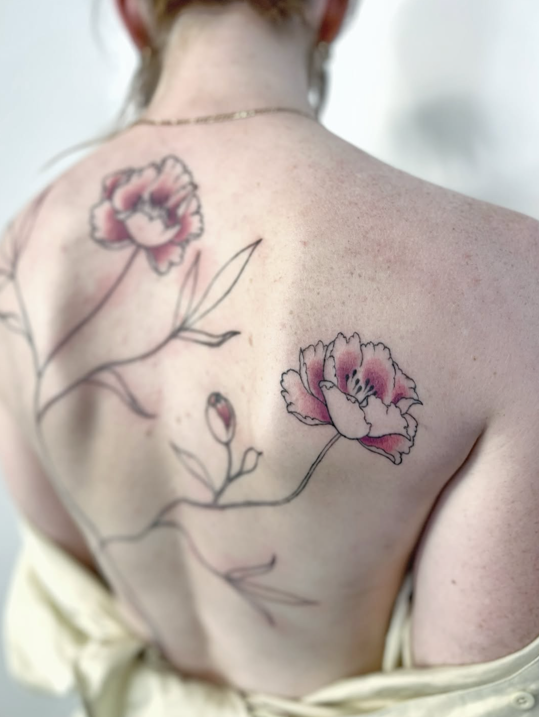 Close-up of a person's back with a floral tattoo featuring pink flowers and black outlines.