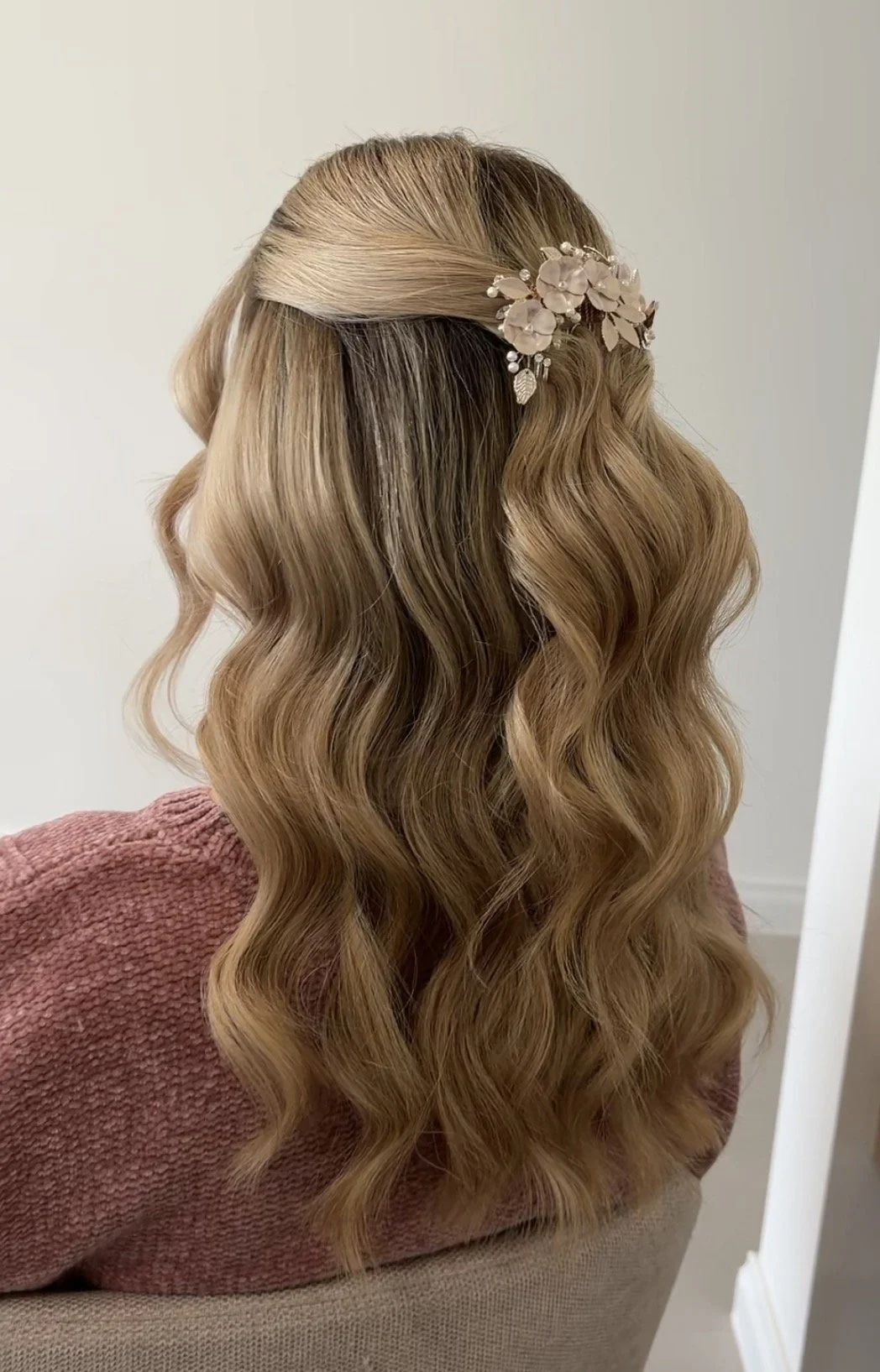 Back view of a woman with long, wavy, light brown hair tied at the top with a decorative floral hair accessory.