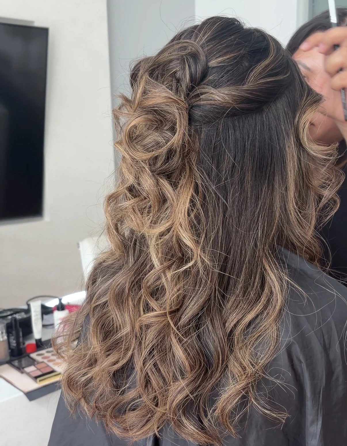 Woman with styled, curly hair in shades of brown and blonde, seen at a hair salon.