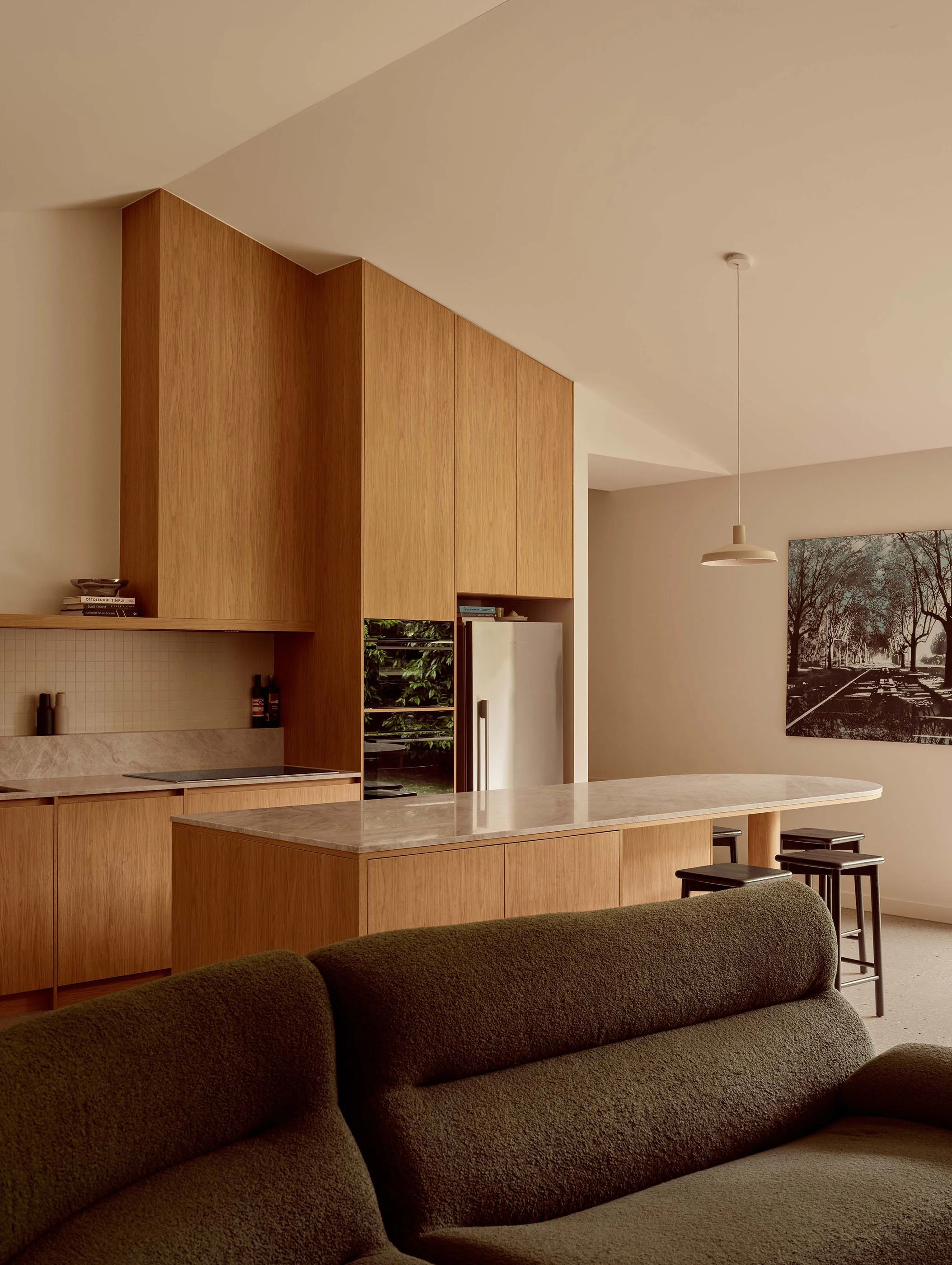 Modern kitchen with beige walls, wooden cabinets, marble island, and a black-and-white photograph of trees hanging on the wall.