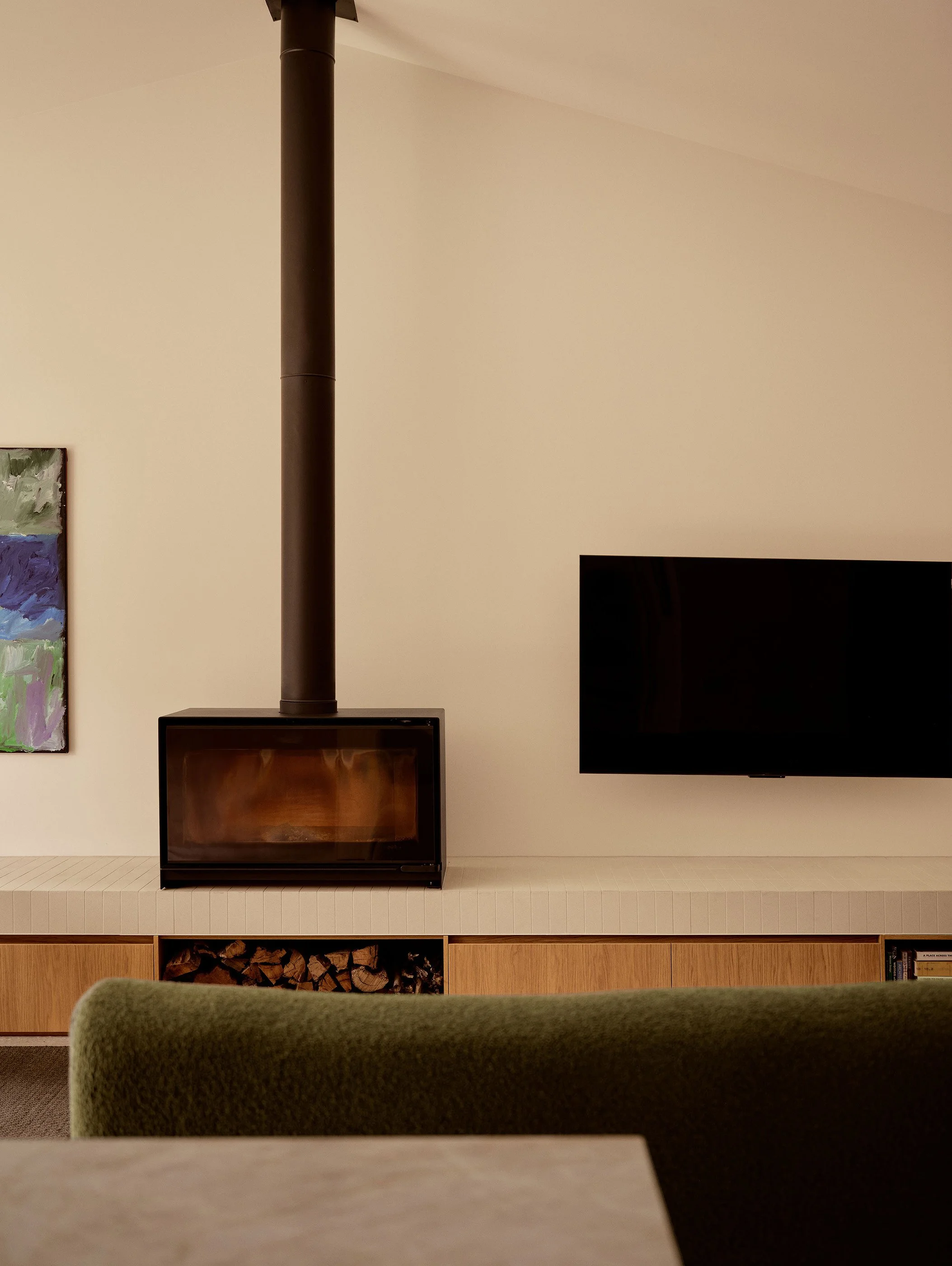 A living room with a wood-burning stove, a TV, a colorful abstract painting, and a green upholstered chair in the foreground.