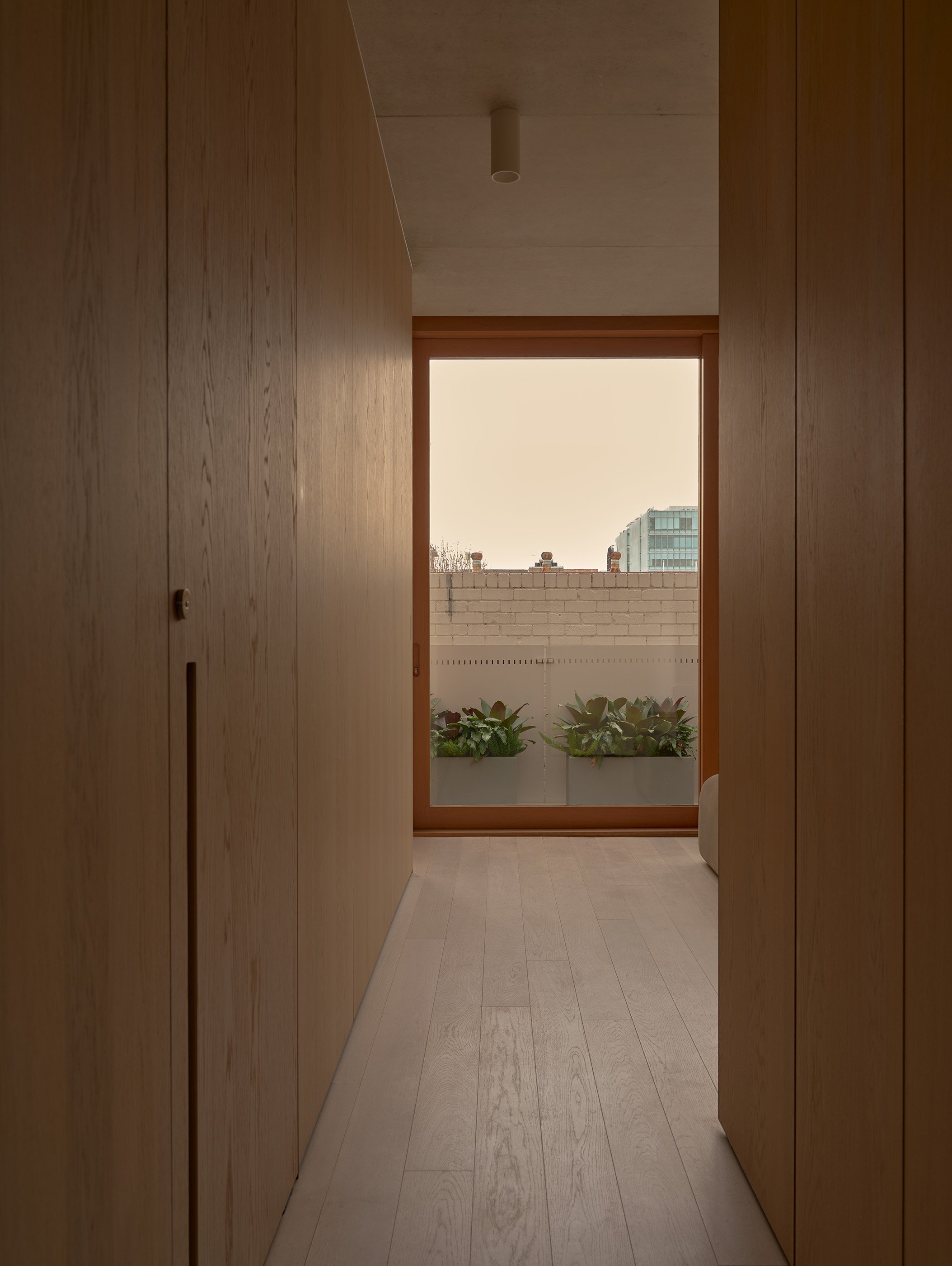 A hallway leading to a patio with potted plants and a city skyline view.