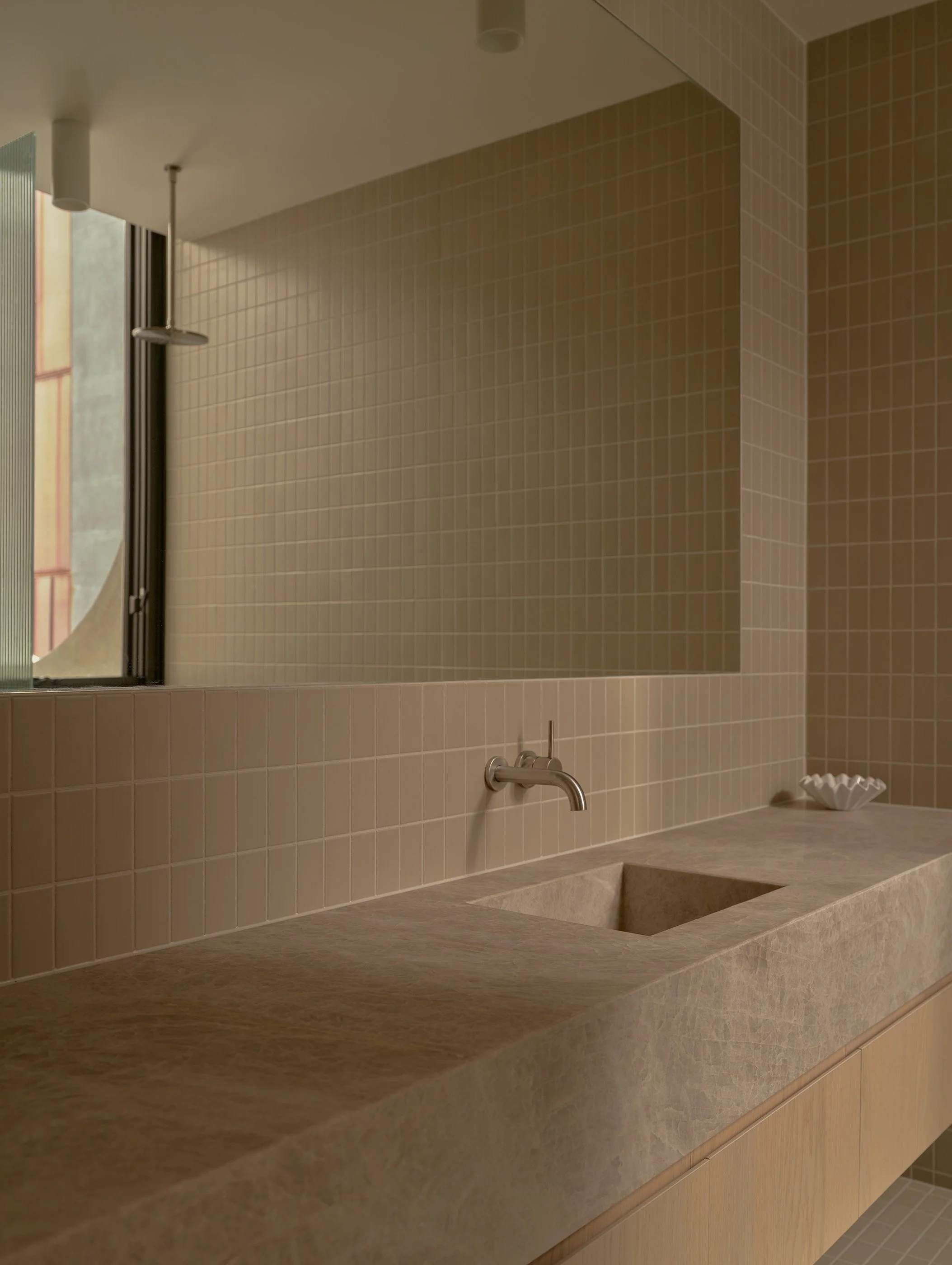 Bathroom with beige tiled wall and a large mirror, countertop with an integrated sink, faucet, and a small white dish.